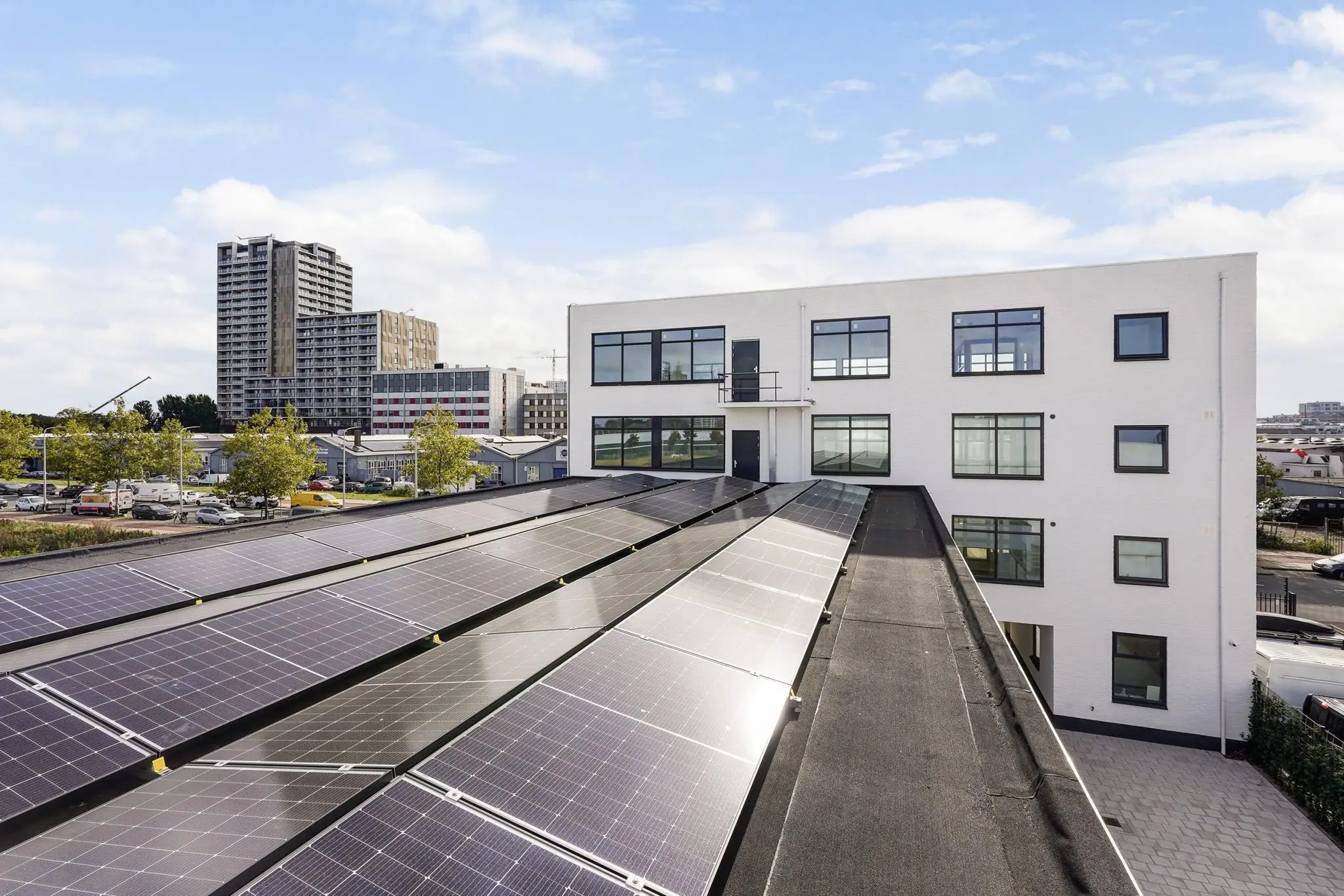 Wit bedrijfsgebouw aan de Mercuriusweg met zonnepanelen op het dak en hoogbouw op de achtergrond.