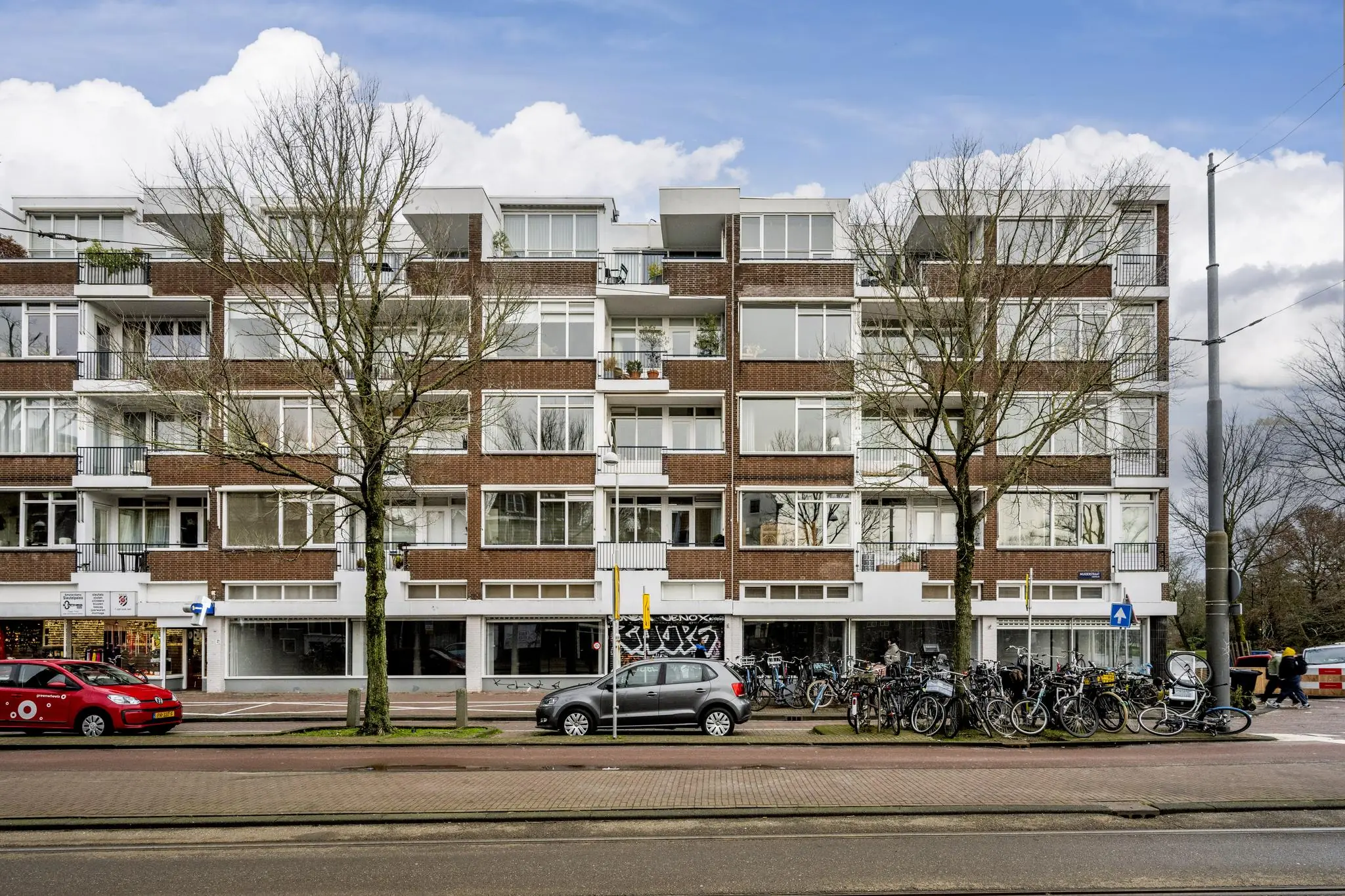 Appartementencomplex aan de Muiderstraat met geparkeerde auto's en fietsen op de voorgrond.
