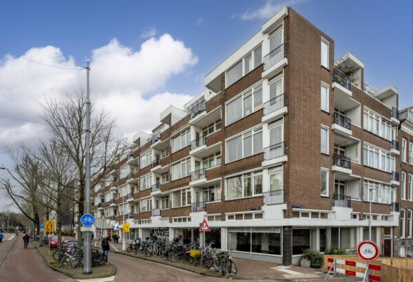 Hoekpand aan de Muiderstraat in Amsterdam met meerdere woonlagen, balkons en geparkeerde fietsen langs de stoep.
