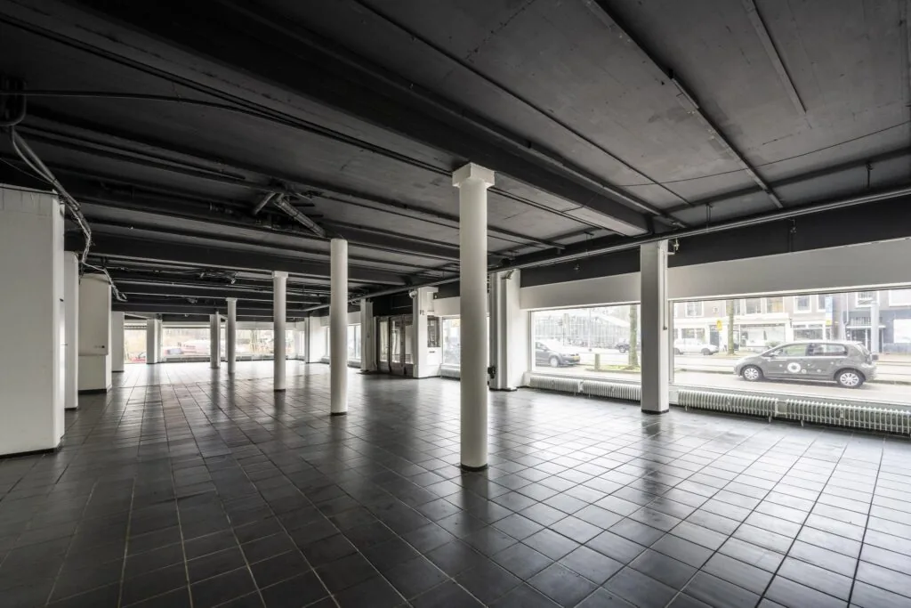 Leegstaand bedrijfspand aan de Muiderstraat met zwarte tegelvloer, witte kolommen en grote etalageramen aan de straatzijde.