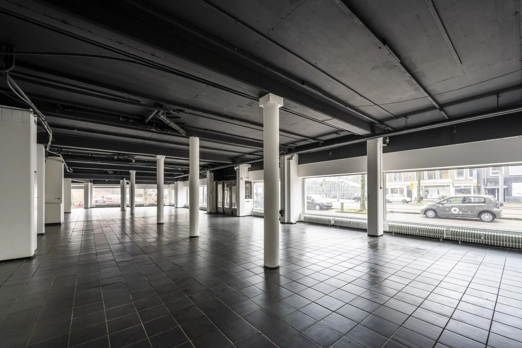 Leegstaand bedrijfspand aan de Muiderstraat met zwarte tegelvloer, witte kolommen en grote etalageramen aan de straatzijde.