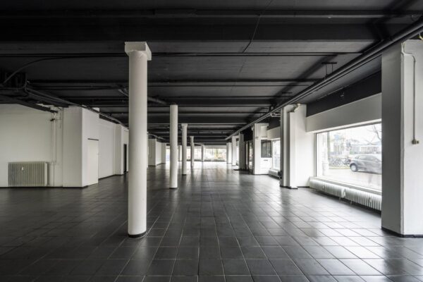 Leegstaand bedrijfs- of winkelpand aan de Muiderstraat met zwarte tegelvloer, witte pilaren en grote etalageramen.