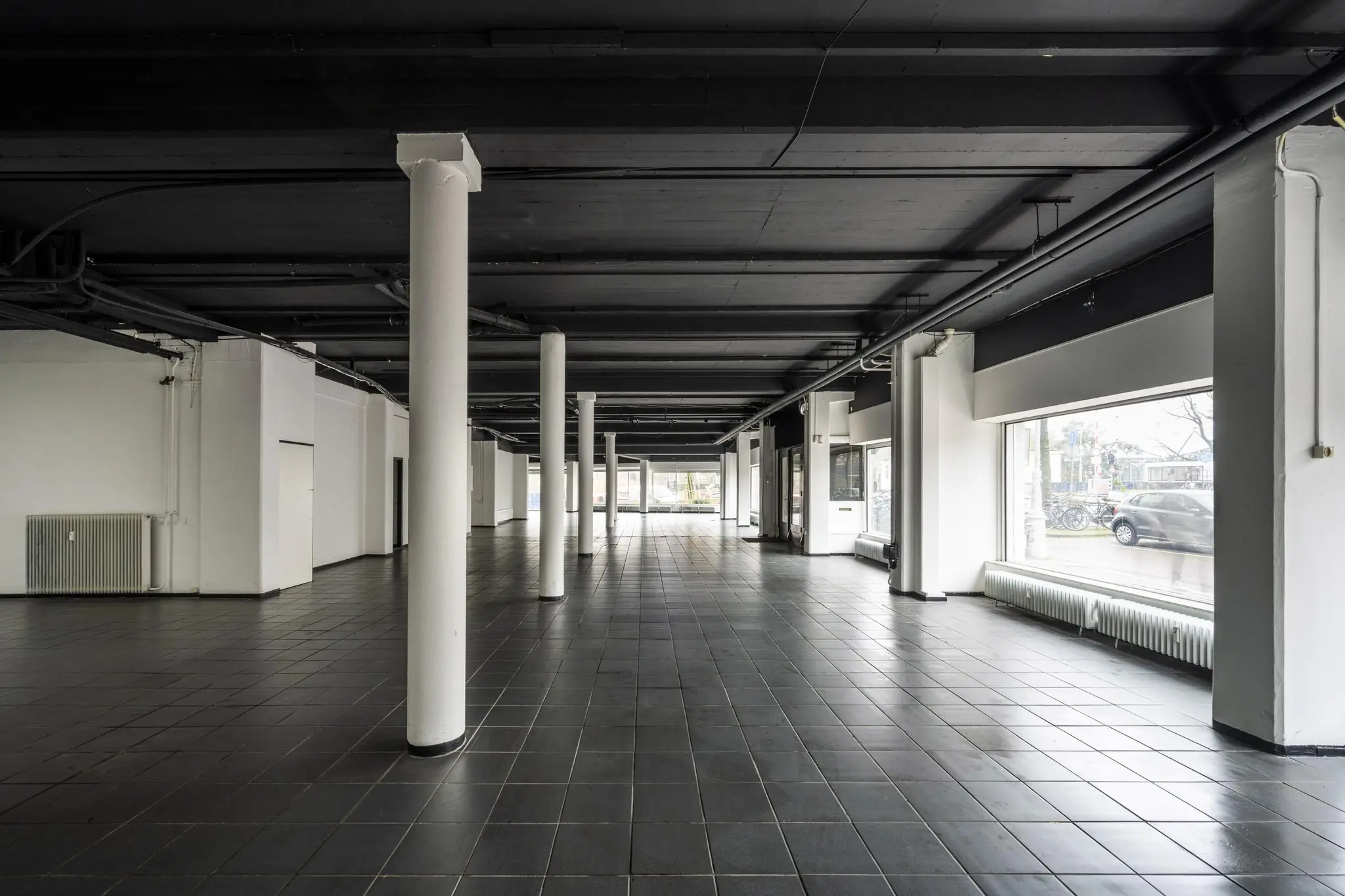 Leegstaand bedrijfs- of winkelpand aan de Muiderstraat met zwarte tegelvloer, witte pilaren en grote etalageramen.