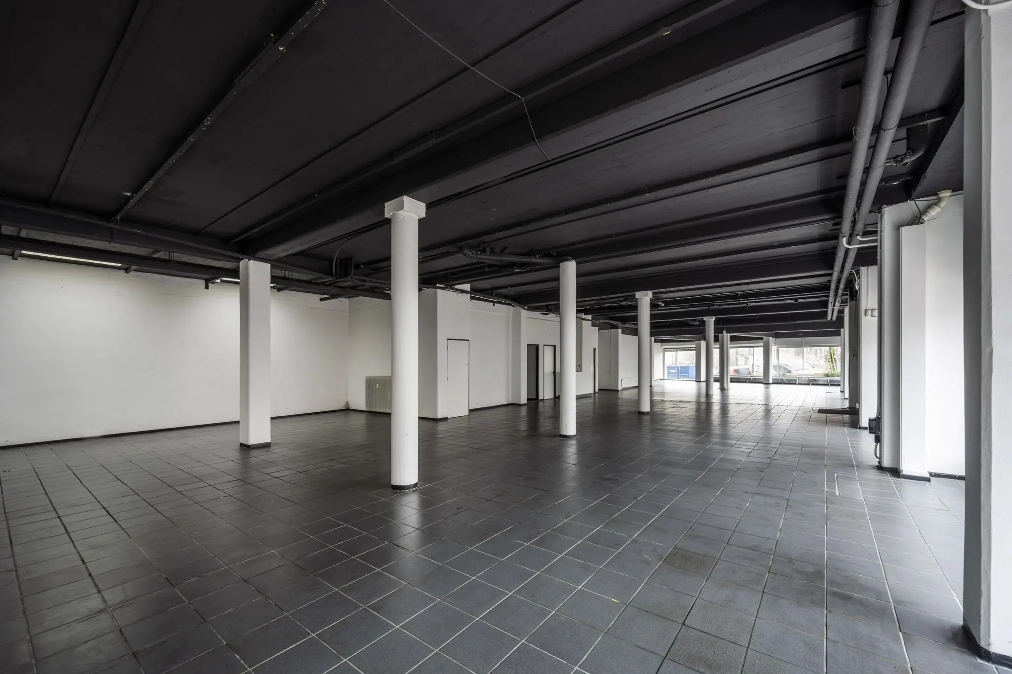 Leeg bedrijfspand aan de Muiderstraat met zwarte tegelvloer, witte pilaren en grote ramen aan de straatzijde.