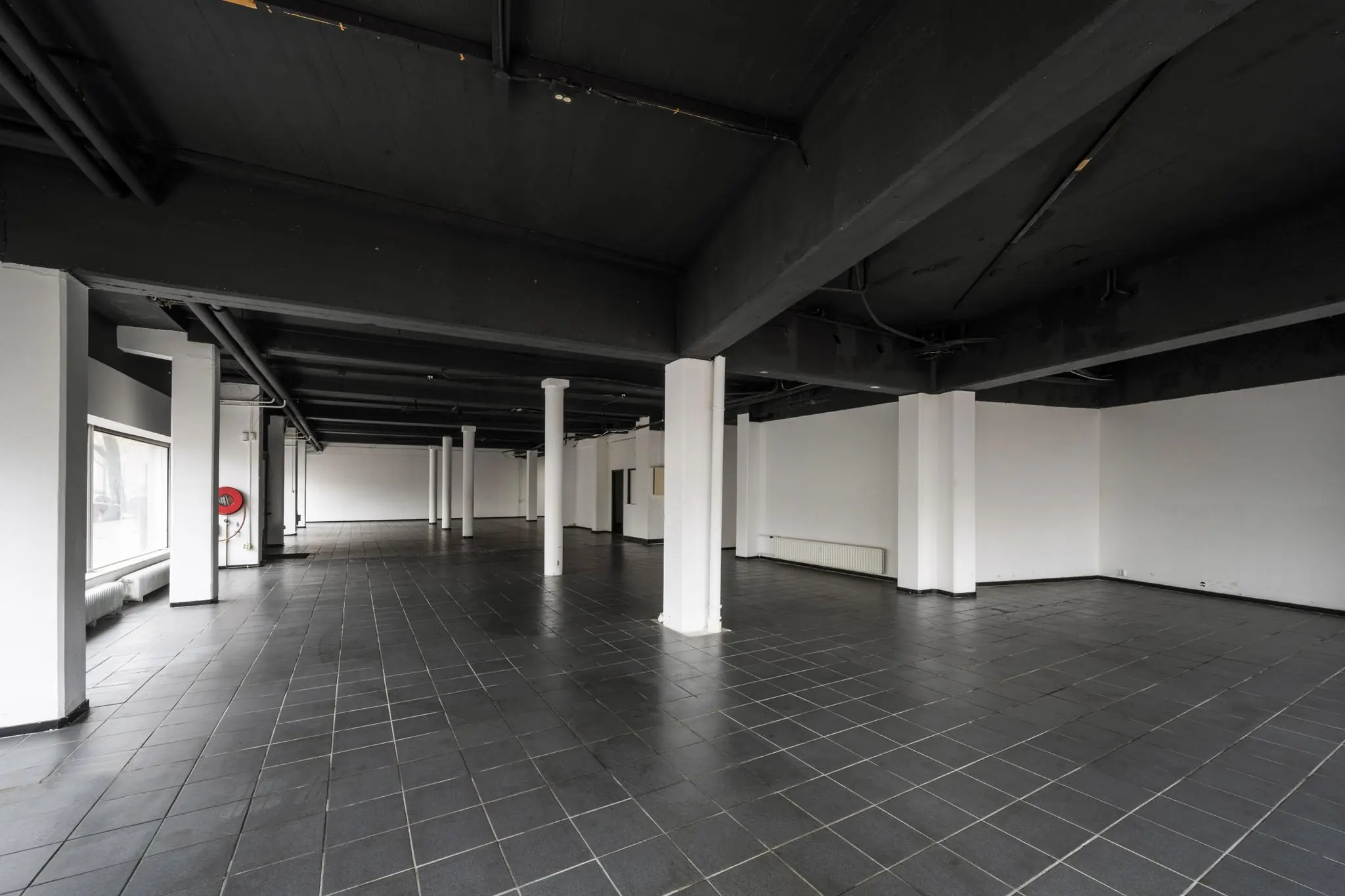 Leegstaand, industrieel ogend interieur van een pand aan de Muiderstraat met zwarte plafondbalken en donkere tegelvloer.