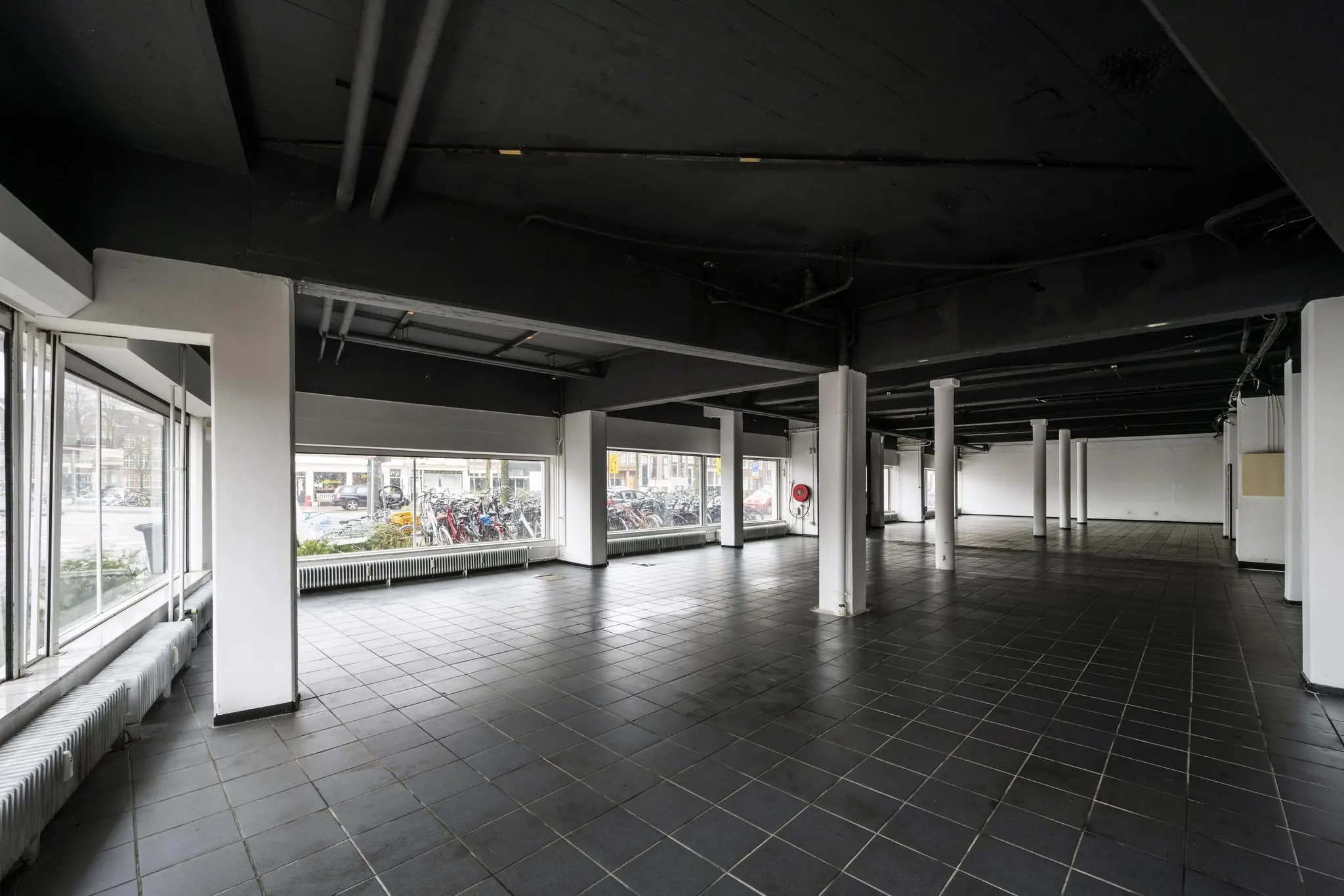 Leegstaand bedrijfspand aan de Muiderstraat met grote ramen en zwarte tegelvloer.