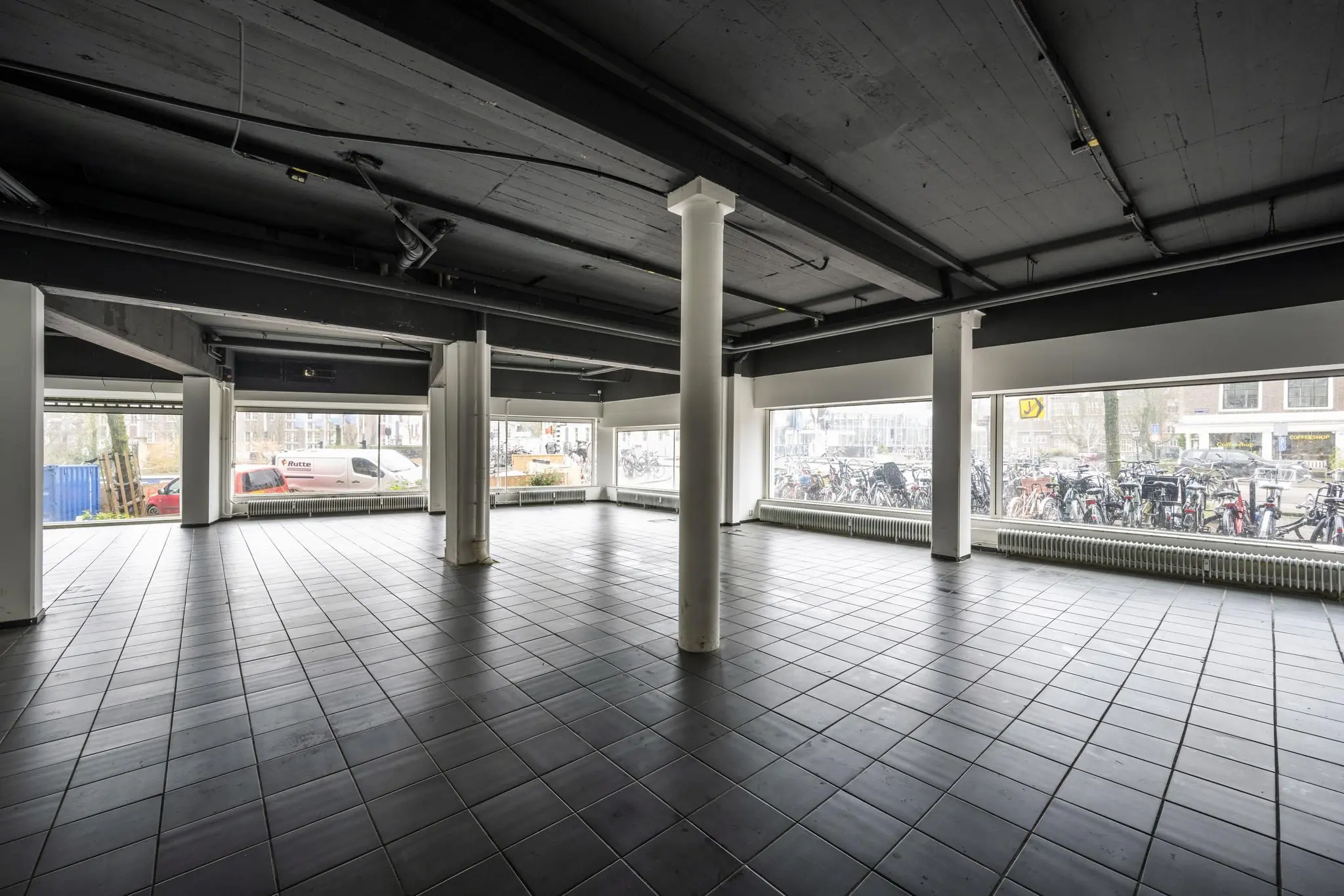 Leeg bedrijfsruimte aan de Muiderstraat met grote ramen en zwart betegelde vloer.