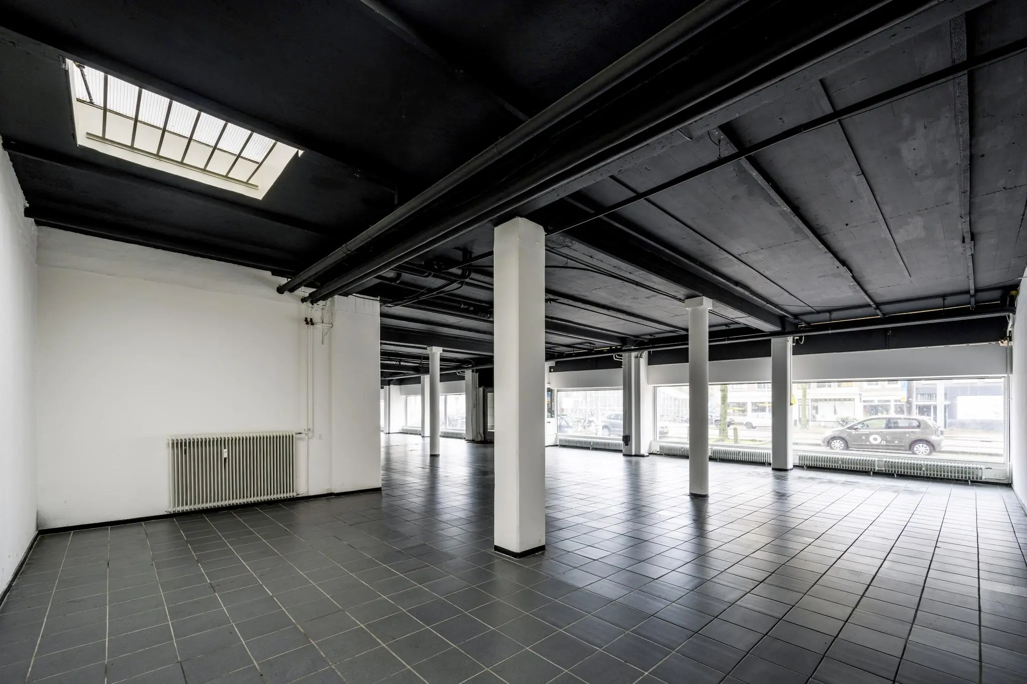 Leeg commercieel pand aan de Muiderstraat met zwarte plafondbalken, witte zuilen en grote ramen aan de straatzijde.