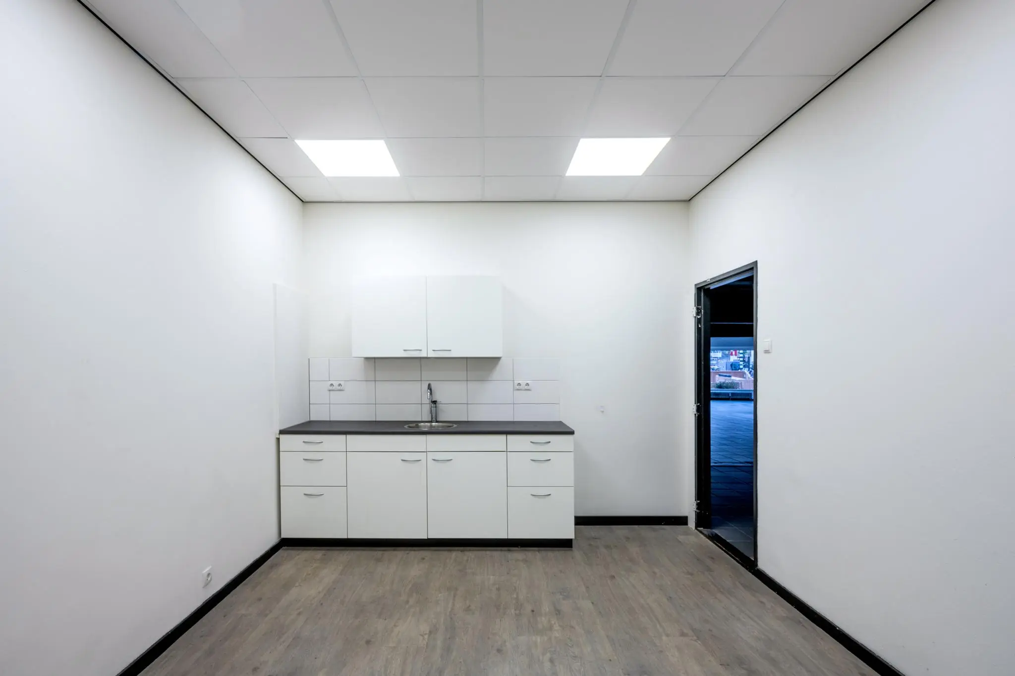 Kleine, witte keuken met boven- en onderkasten, een wasbak en een deur naar buiten in een strak afgewerkte ruimte op de Muiderstraat.