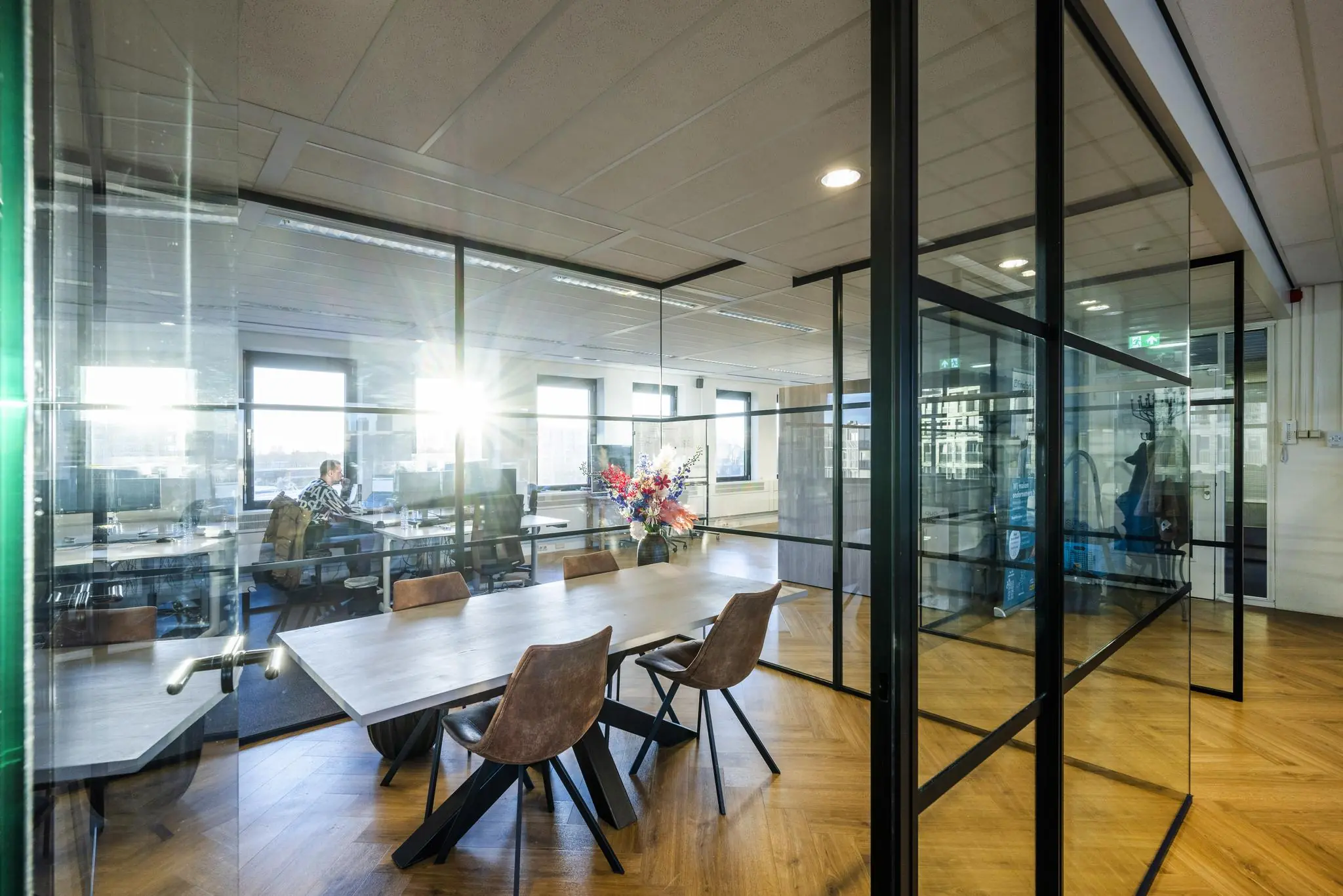 Moderne kantoorruimte aan de Radarweg met glazen vergaderruimte, houten vloer en werkplekken met computers.