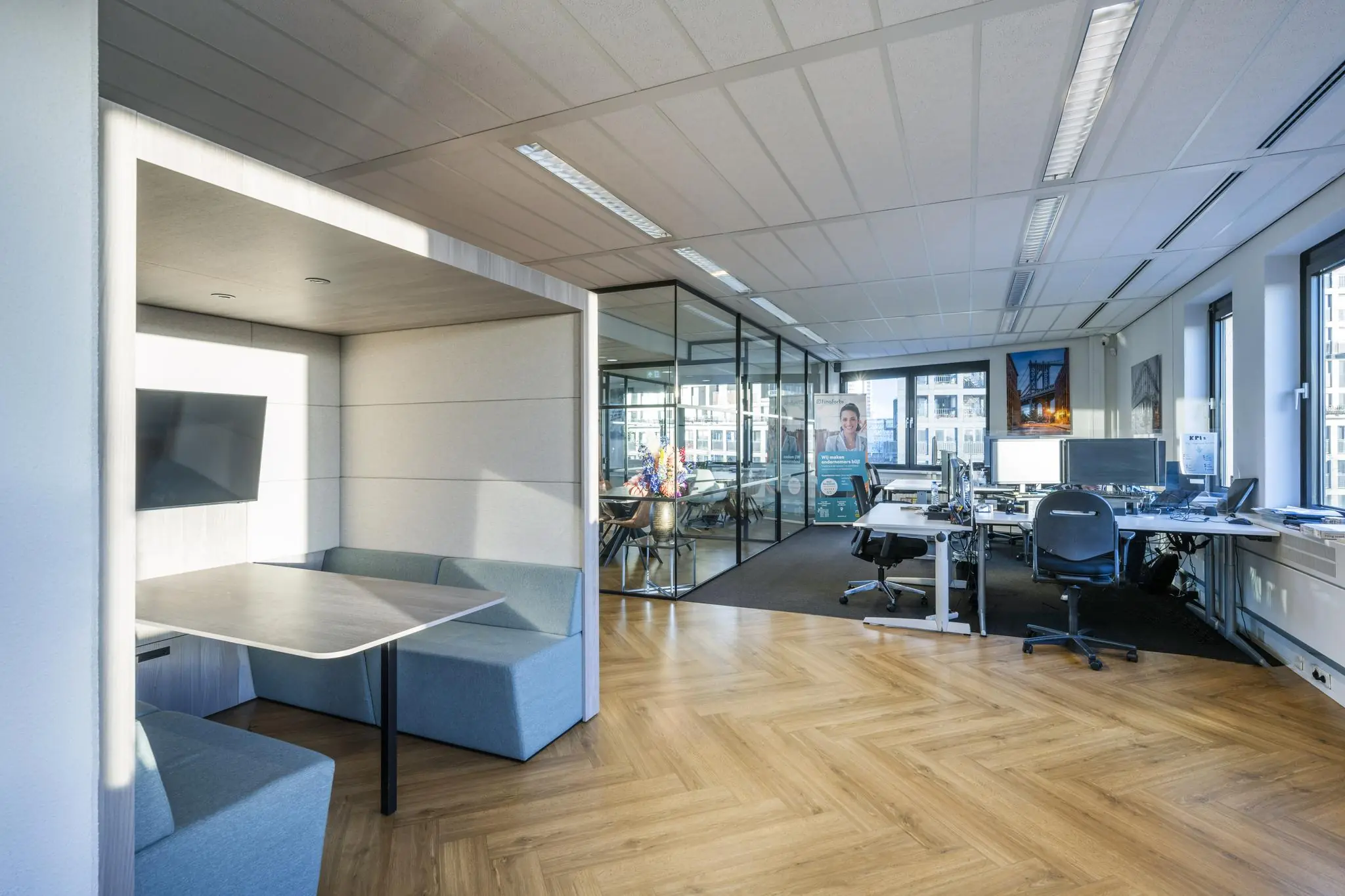 Modern kantoorinterieur aan de Radarweg met glazen vergaderruimte, werkplekken en een zitnis met tv-scherm.