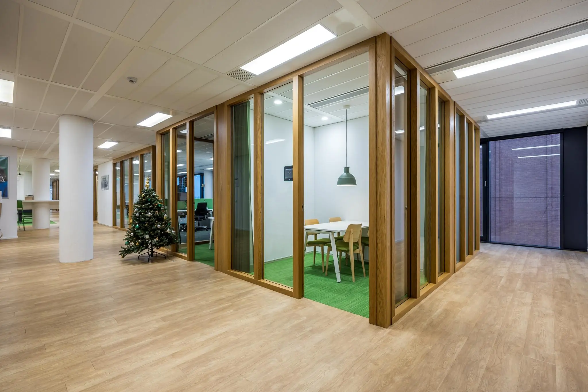 Moderne kantoorruimte aan de Winthontlaan met glazen vergaderruimtes, houten details en een versierde kerstboom.