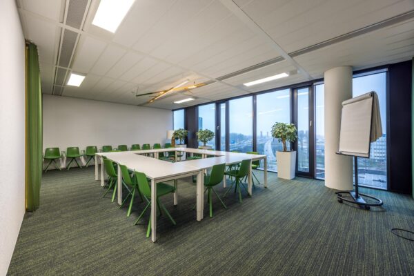 Vergaderruimte aan de Winthontlaan met groene stoelen, U-vormige opstelling, flip-over en uitzicht op de snelweg.