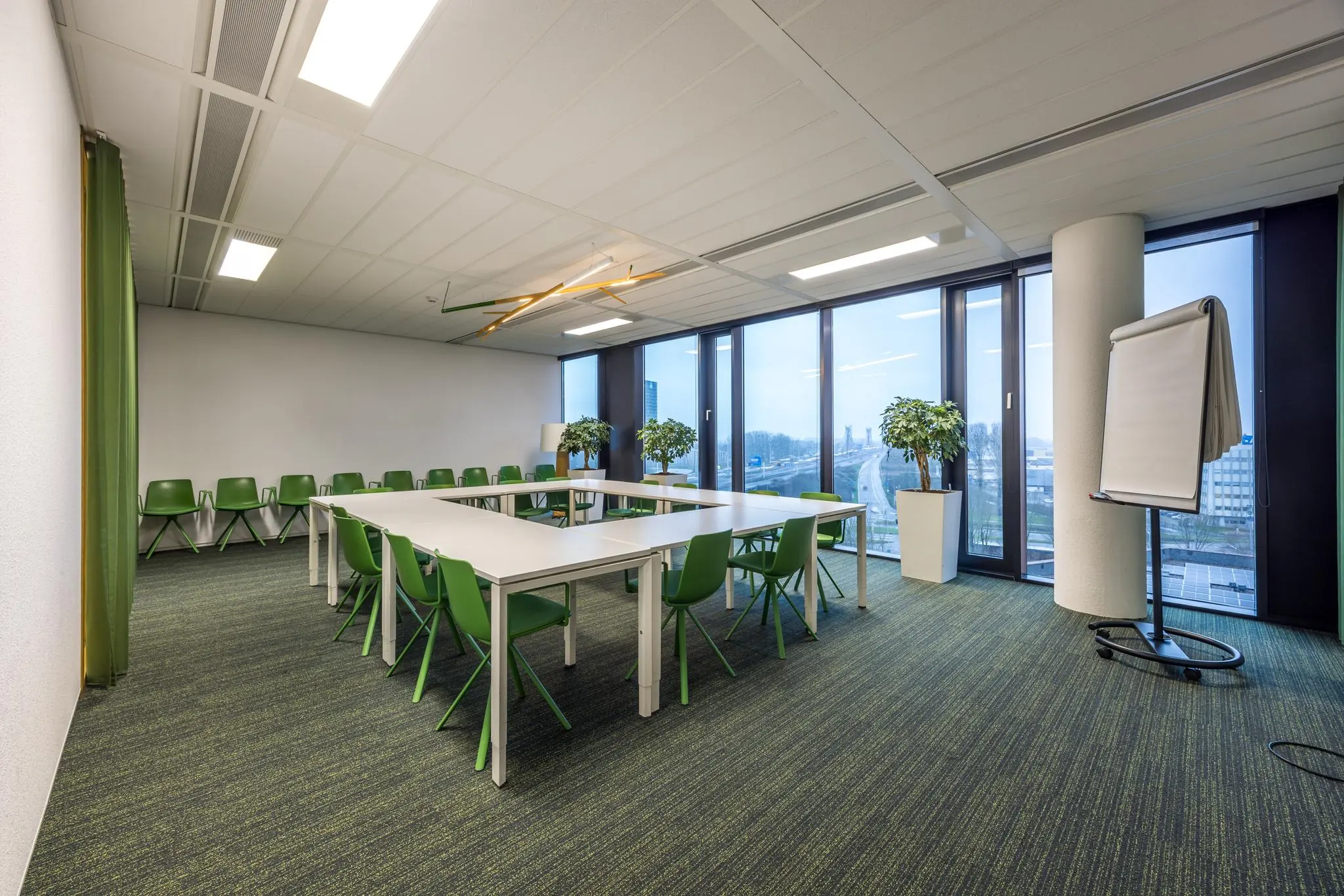 Vergaderruimte aan de Winthontlaan met groene stoelen, U-vormige opstelling, flip-over en uitzicht op de snelweg.