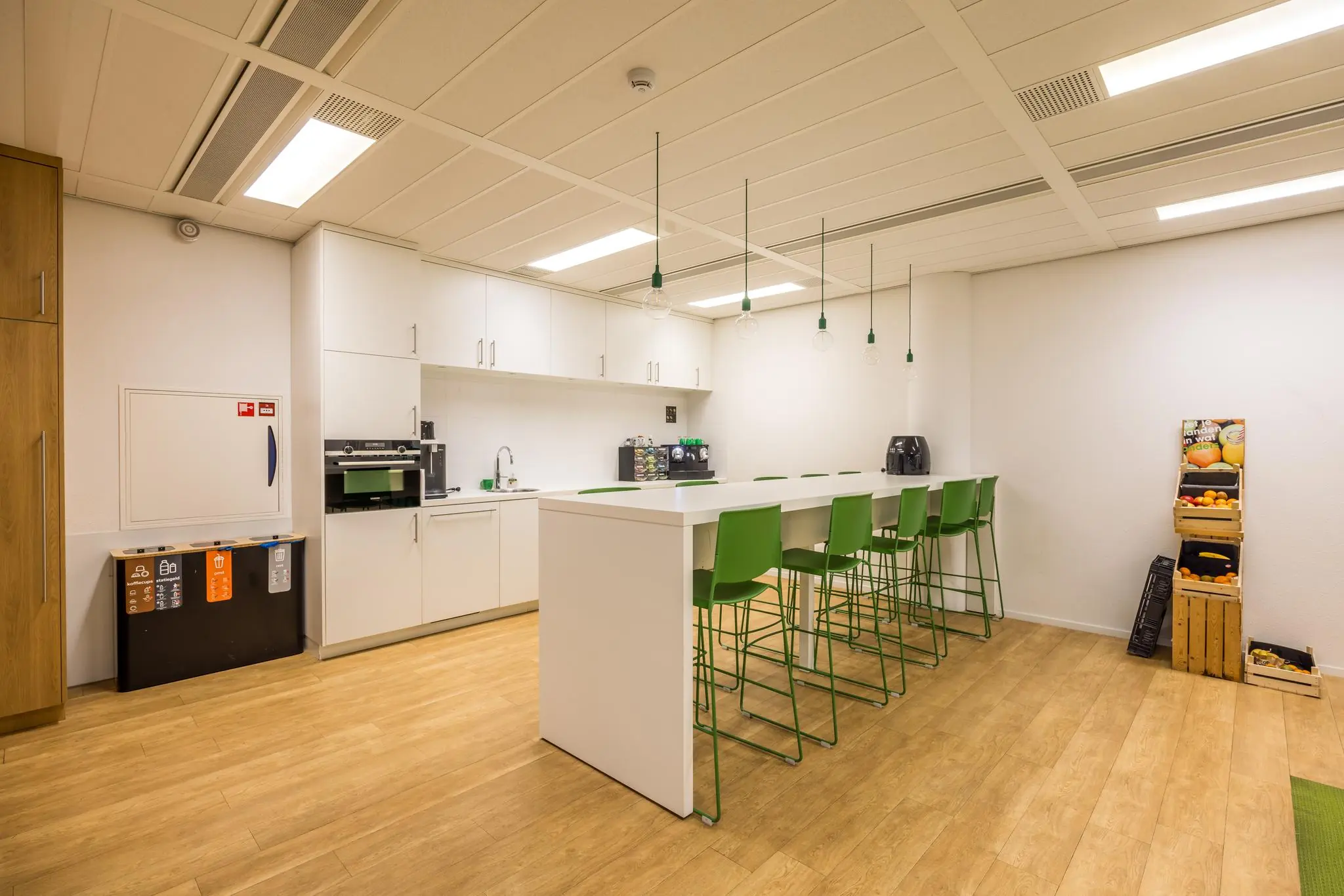 Moderne kantoorkeuken aan de Winthontlaan met witte kasten, groene barkrukken en een fruitrek in de hoek.