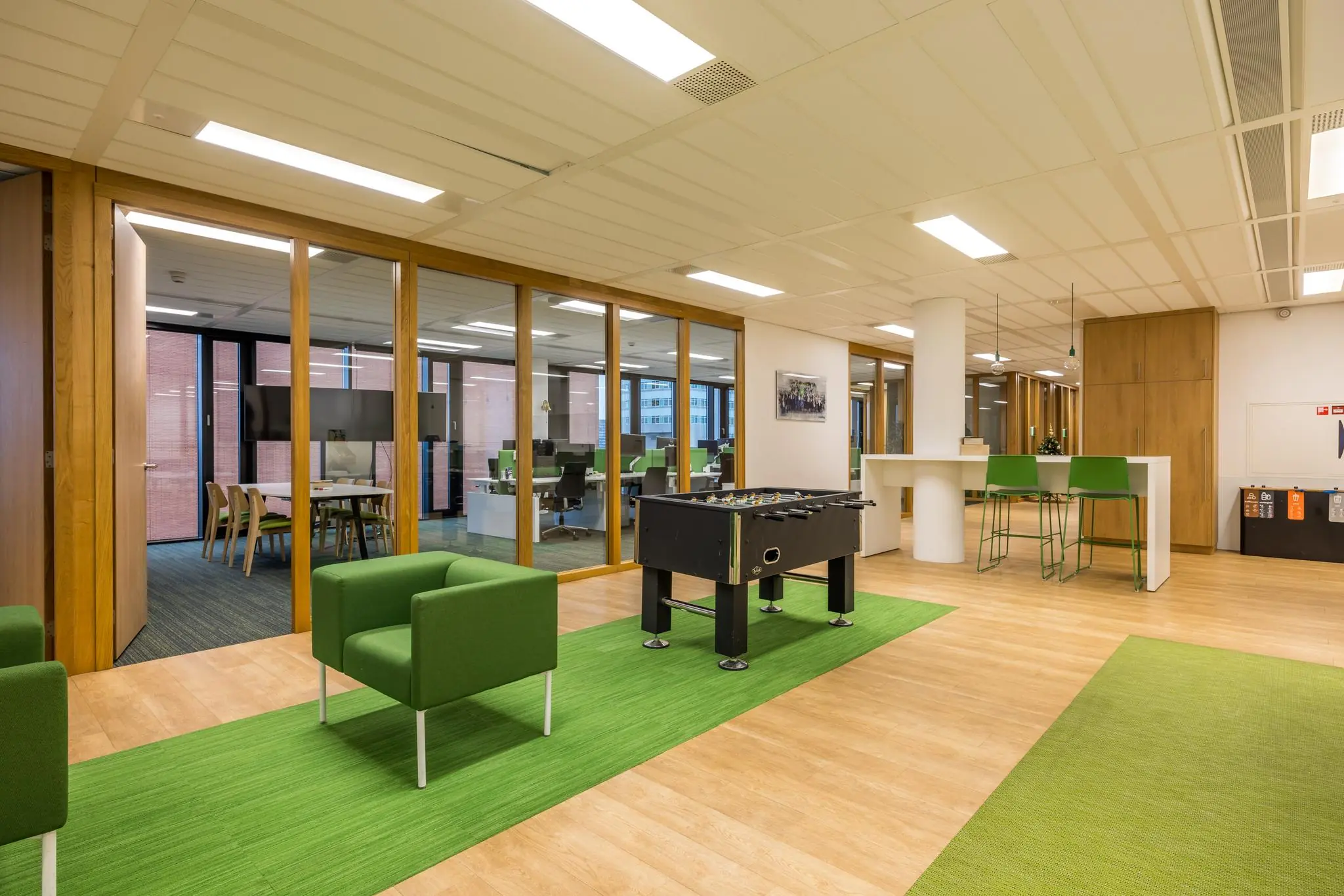 Moderne kantoorruimte aan de Winthontlaan met groene accenten, glazen vergaderruimtes en een tafelvoetbaltafel.