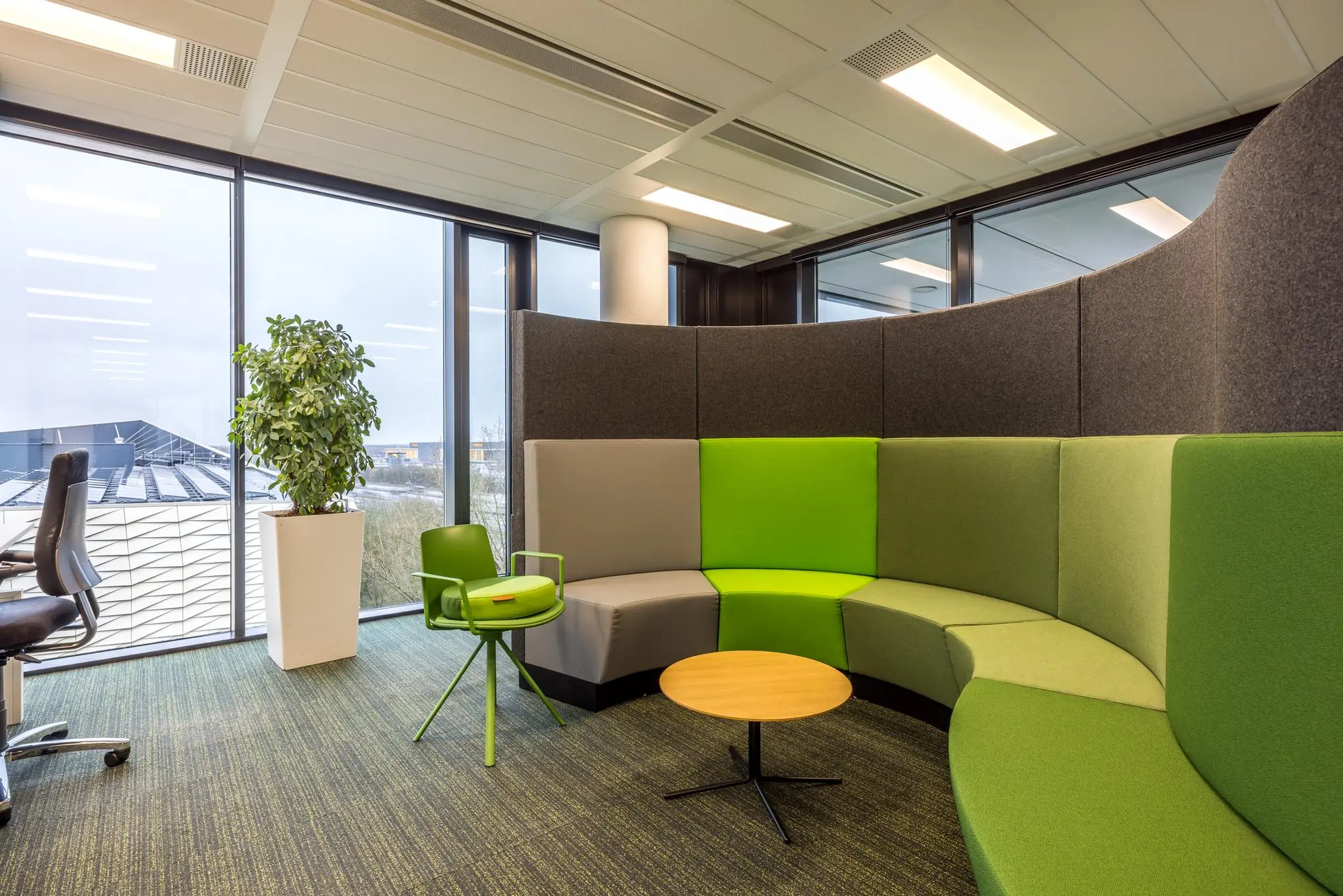 Moderne kantoorlounge aan de Winthontlaan met ronde groene zithoek, plant en grote ramen.