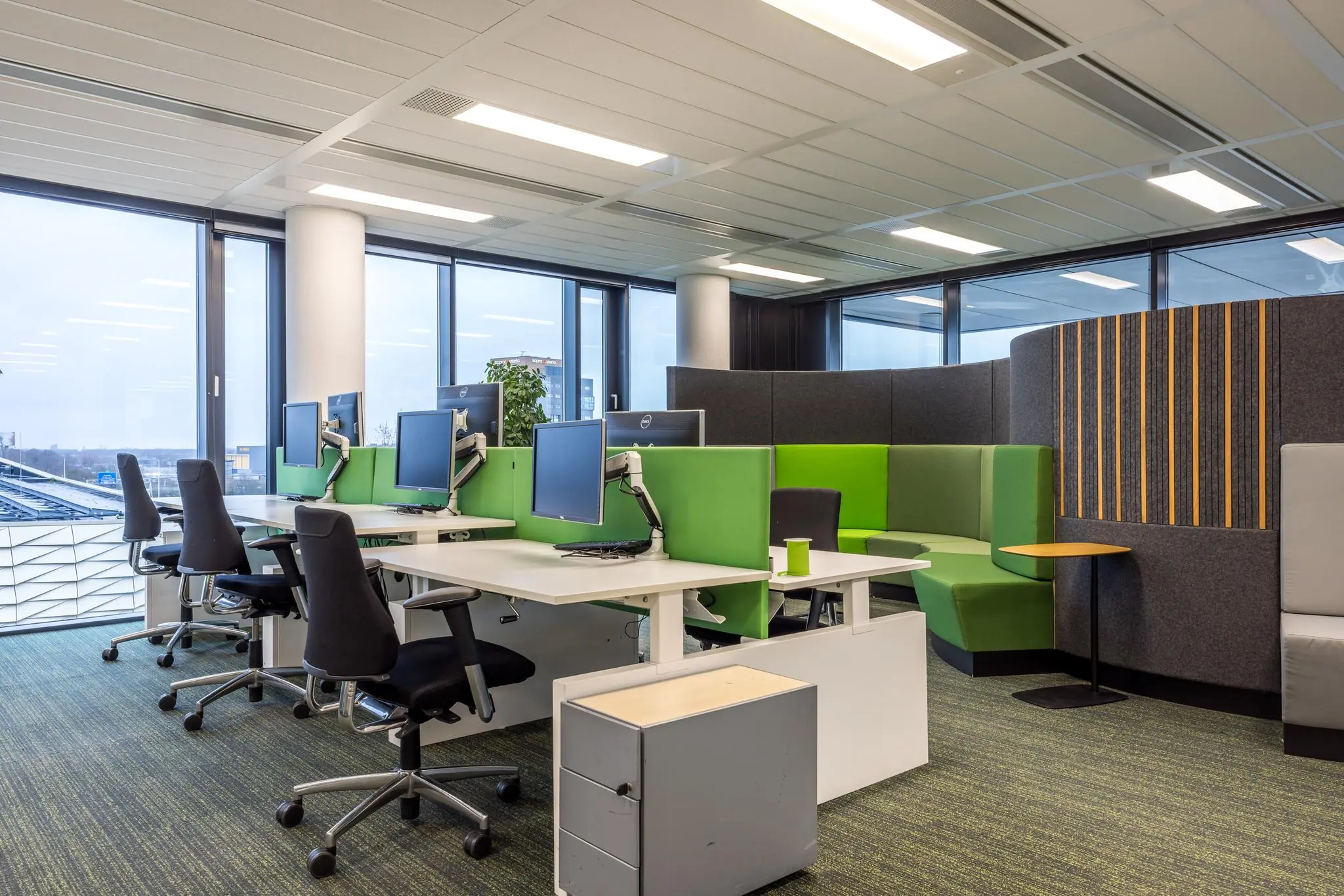 Moderne kantoorruimte aan de Winthontlaan met werkplekken, ergonomische stoelen en een zithoek met groene en grijze akoestische panelen.