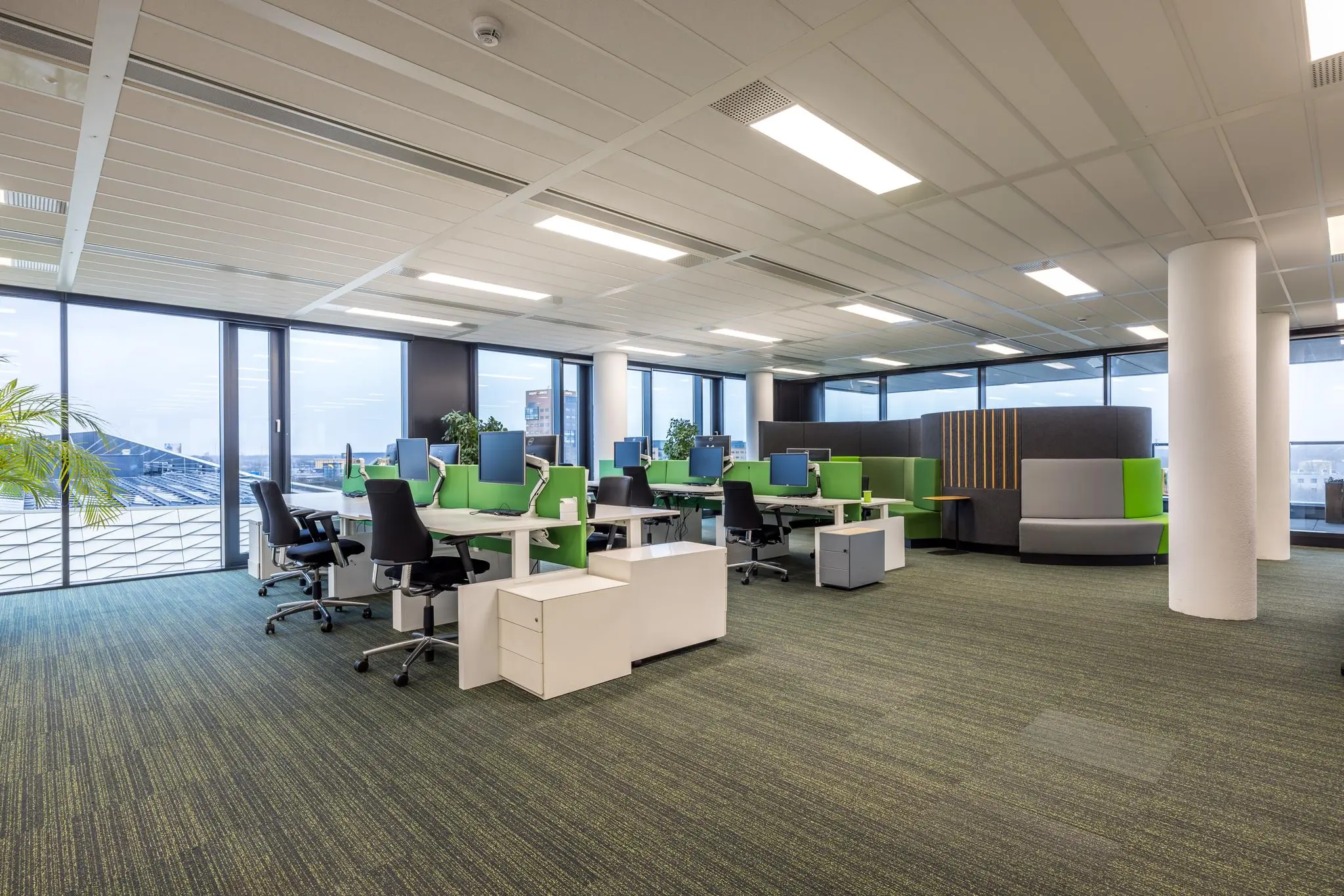 Modern kantoorpand aan de Winthontlaan met een open werkruimte, groene bureauschermen en panoramisch uitzicht.