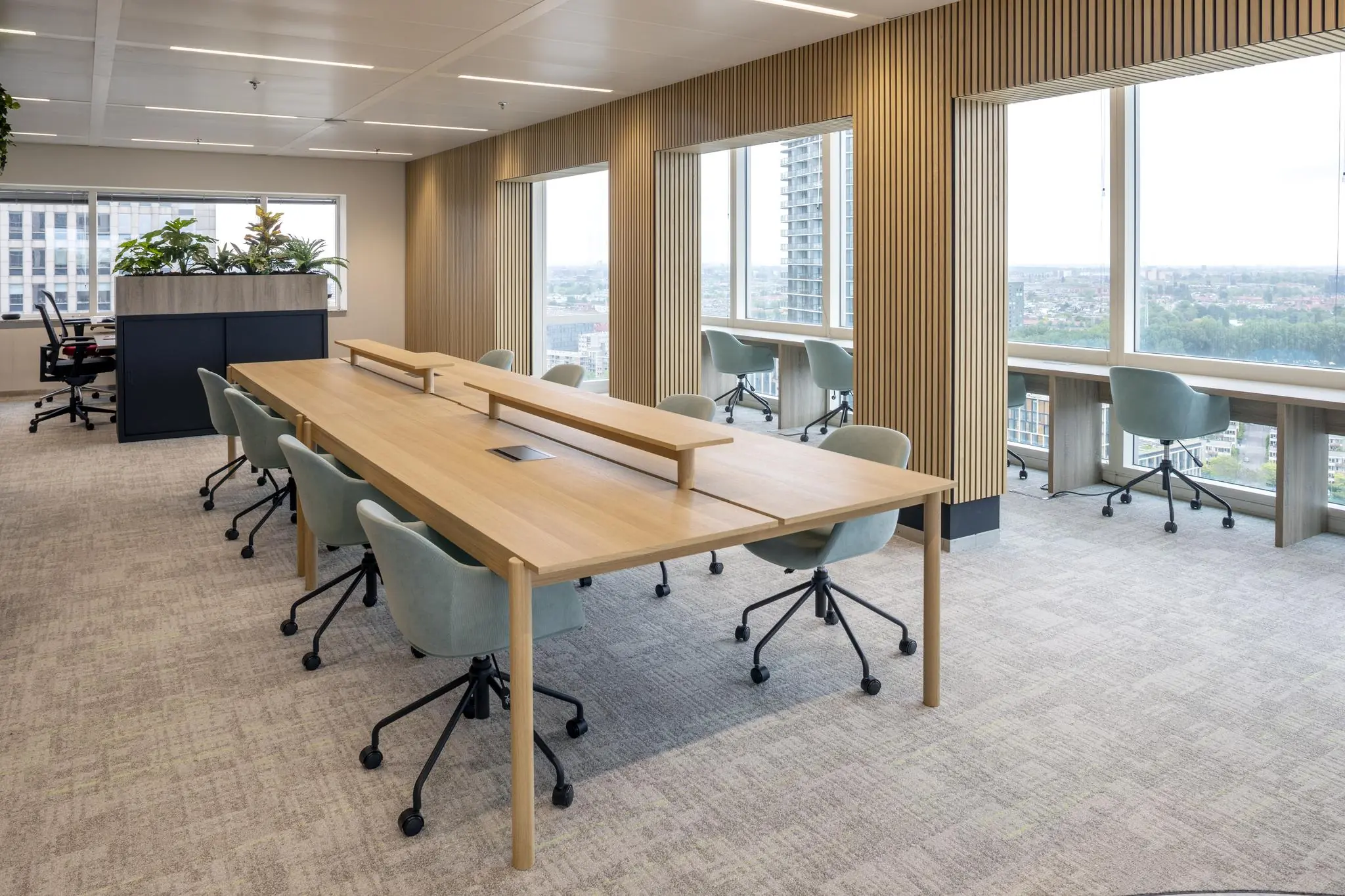Modern kantoorinterieur op Amstelplein met houten werktafels, bureaustoelen en uitzicht op de stad.