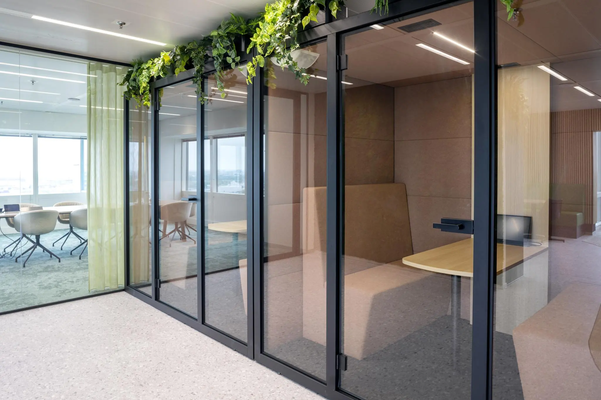 Moderne kantoorruimte aan het Amstelplein met glazen vergaderruimtes, akoestische belcel en hangende planten.