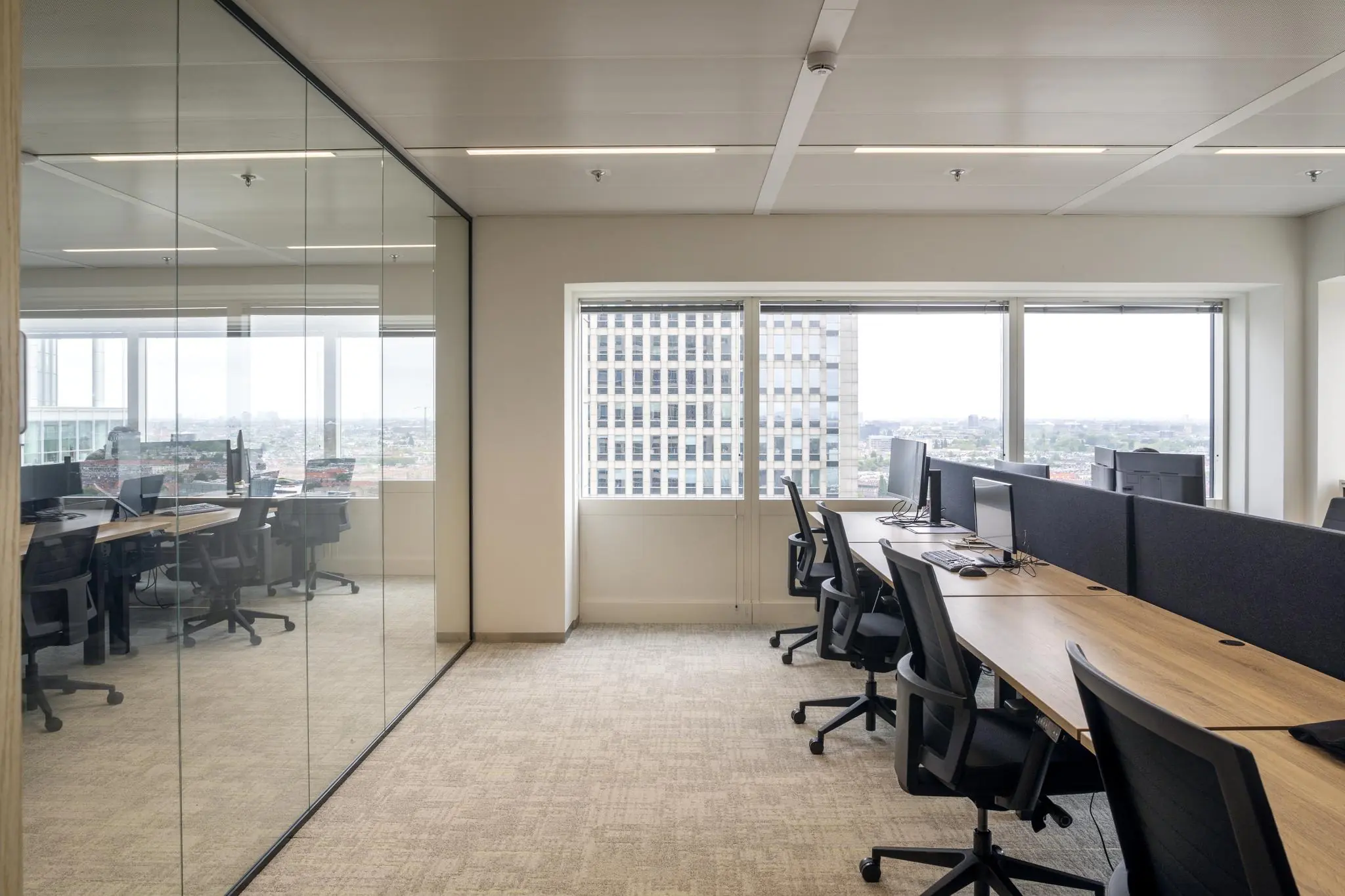 Moderne kantoortuin aan het Amstelplein met werkplekken, computers en uitzicht op een hoog gebouw.