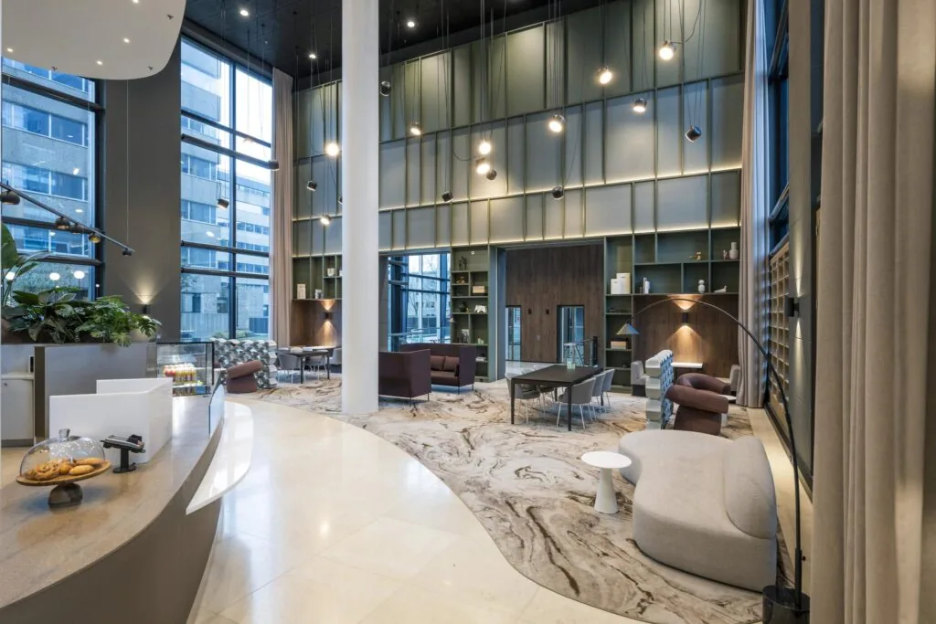 Moderne en stijlvolle lobby van een kantoorgebouw aan het Amstelplein, met hoge plafonds, grote ramen en diverse zitgelegenheden.