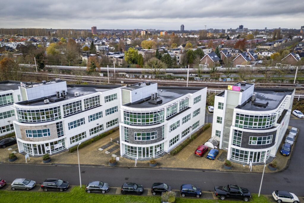 Luchtfoto van het kantoorpand Rhijnspoor in een stedelijke omgeving met spoorlijn op de achtergrond.