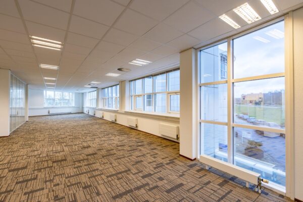 Lichte, ruime kantoorruimte in het gebouw Rhijnspoor met grote ramen en tapijtvloer.