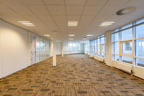 Lichte, ruime kantoorruimte in het Rhijnspoor-gebouw met grote ramen en tapijtvloer.