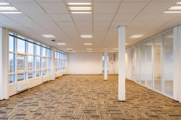 Licht en ruim kantoorinterieur in het Rhijnspoor-gebouw met tapijtvloer, glazen wanden en grote ramen.