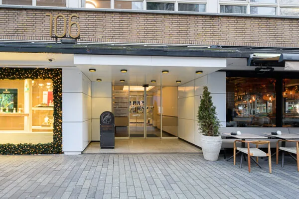 Ingang van een modern kantoorgebouw aan de Meent 106 in Rotterdam, met naastgelegen juwelier en restaurant.