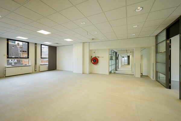 Lichte, lege kantoorruimte aan de Meent met ramen, systeemplafond en gang naar achtergelegen kamers.