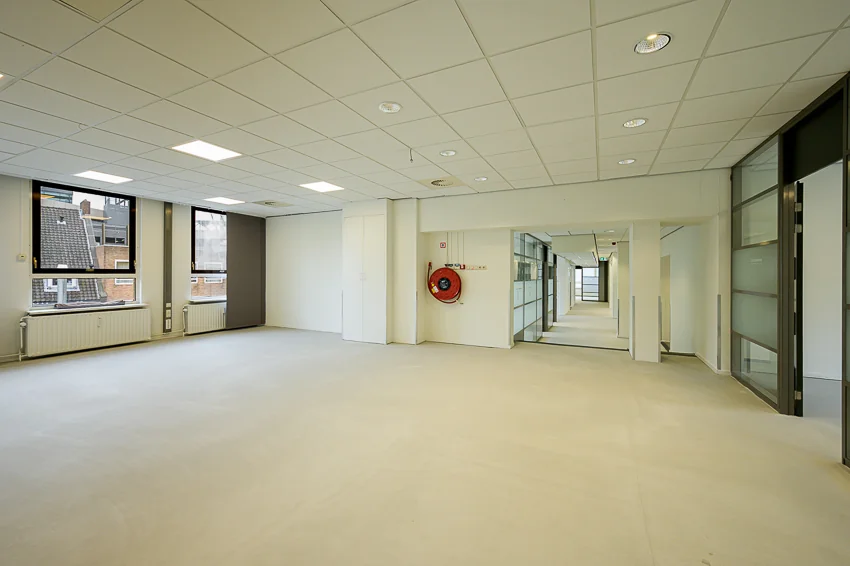 Lichte, lege kantoorruimte aan de Meent met ramen, systeemplafond en gang naar achtergelegen kamers.