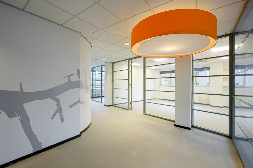 Moderne kantoorruimte op de Meent met glazen wanden, een opvallende oranje plafondlamp en een muurschildering van een tak.
