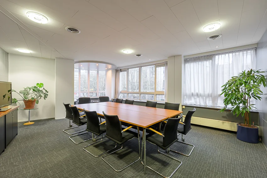 Vergaderruimte Meent met een lange houten tafel, zwarte stoelen en grote ramen die zorgen voor veel daglicht.