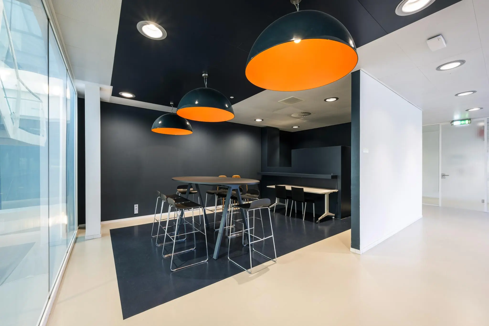Moderne kantoorruimte aan de Prof. E.M. Meijerslaan met hoge tafels, barkrukken en grote zwarte hanglampen met oranje binnenkant.