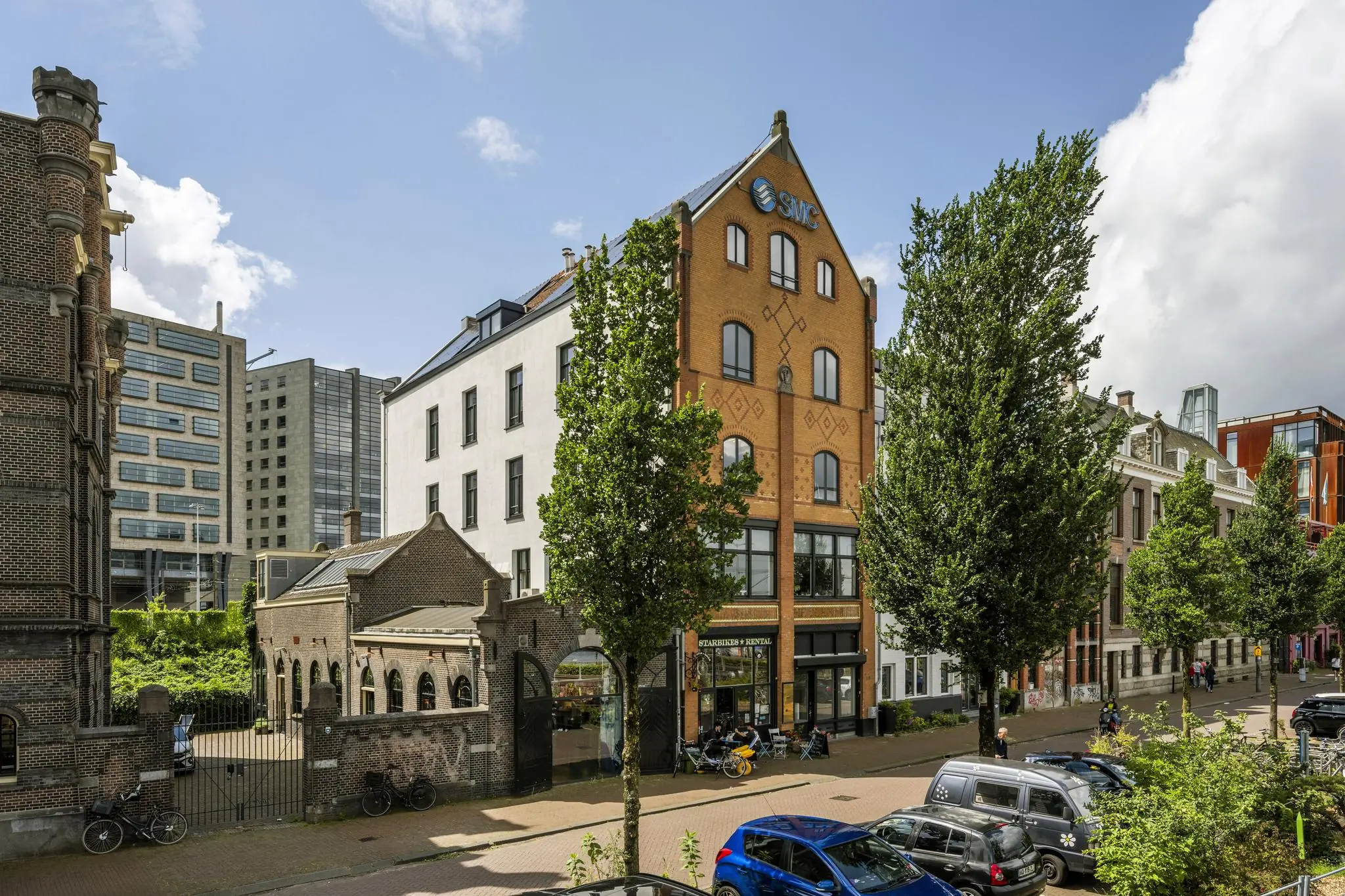 Straatbeeld van de De Ruijterkade in Amsterdam met historische en moderne gebouwen, waaronder het SMC-pand.