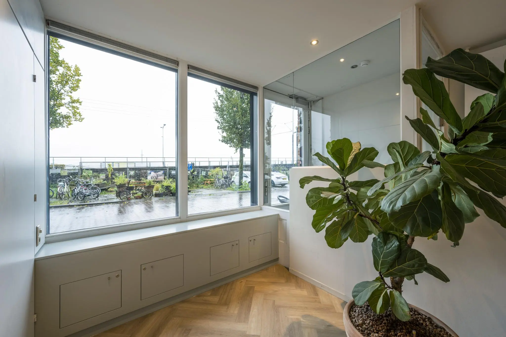 Binnenruimte met grote ramen aan de De Ruijterkade, uitzicht op fietsen en groenstrook buiten.