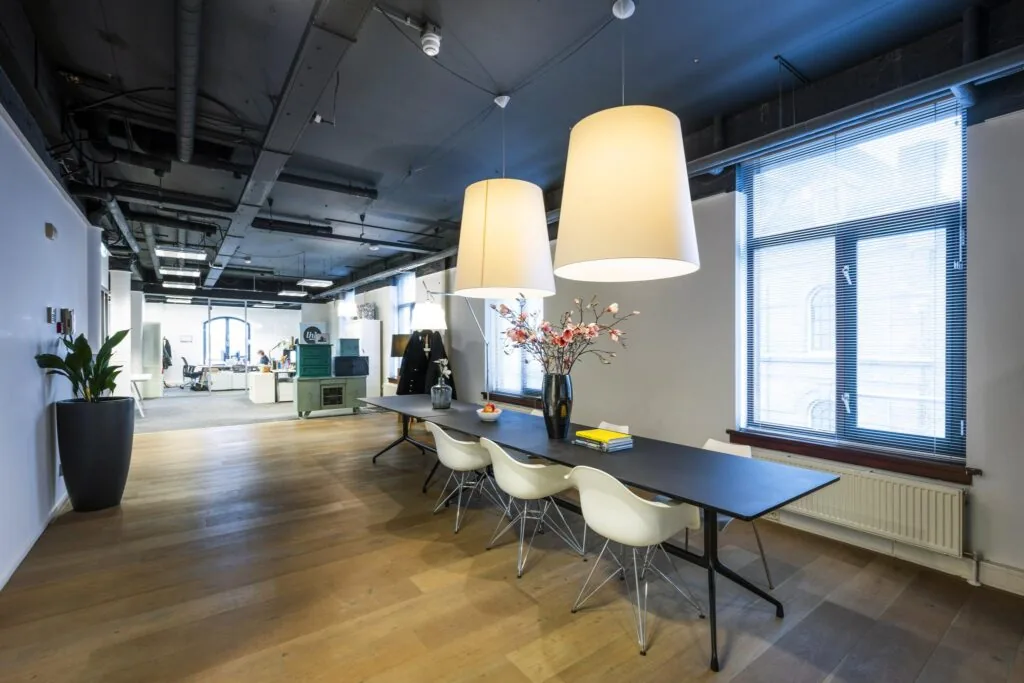 Moderne kantoorruimte aan de De Ruijterkade met een lange tafel, designstoelen, hanglampen en grote ramen.