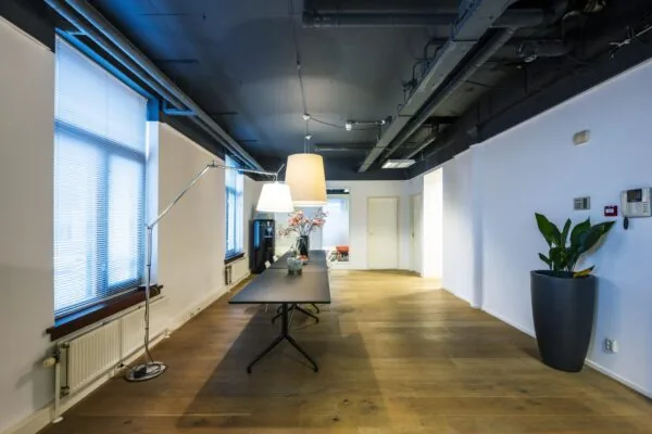 Modern ingericht kantoorinterieur aan de De Ruijterkade met houten vloer, strakke meubels en industriële plafonddetails.