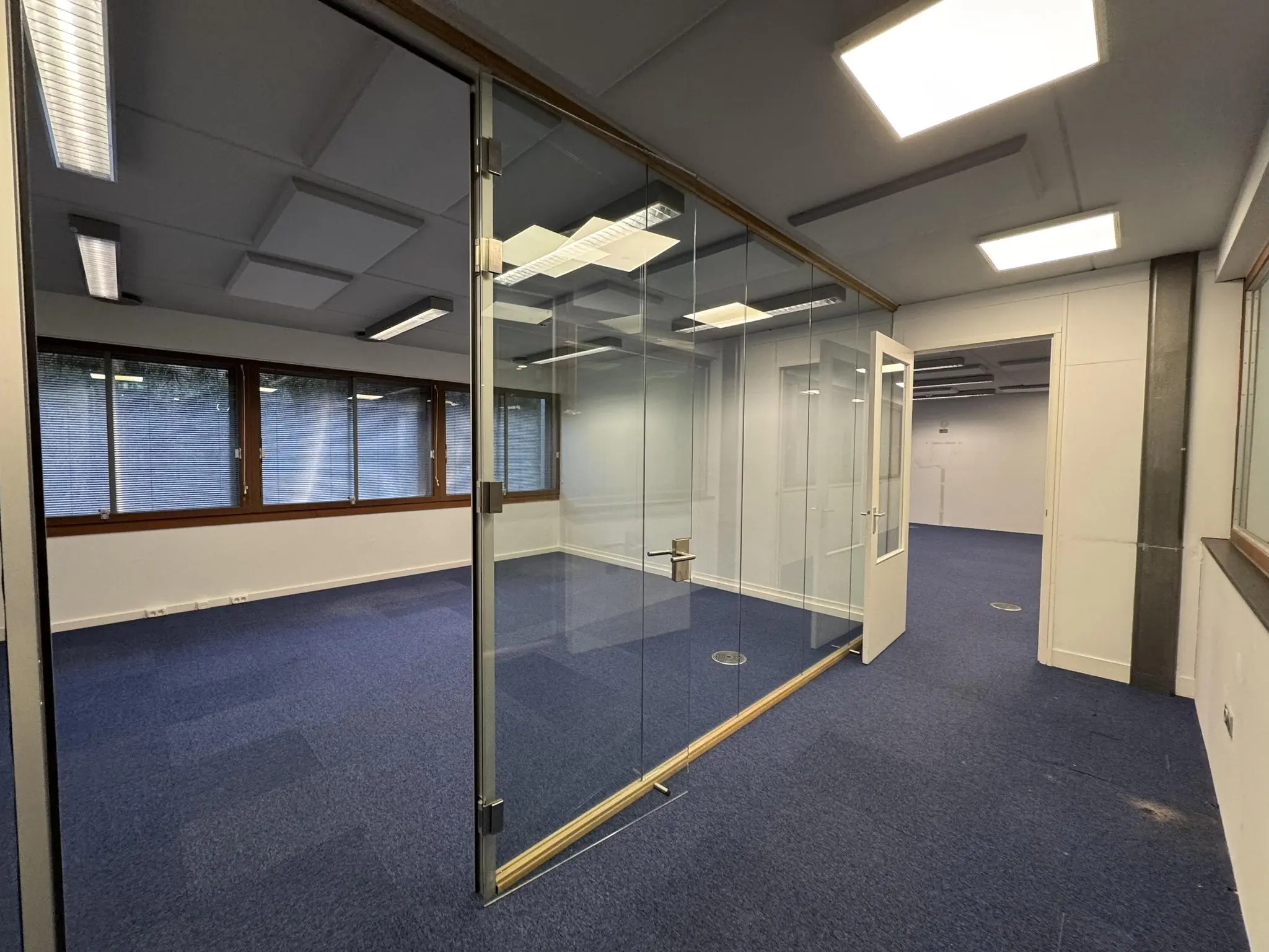 Kantoorruimte aan de De Ruijterkade met glazen vergaderruimte en blauwe vloerbedekking.