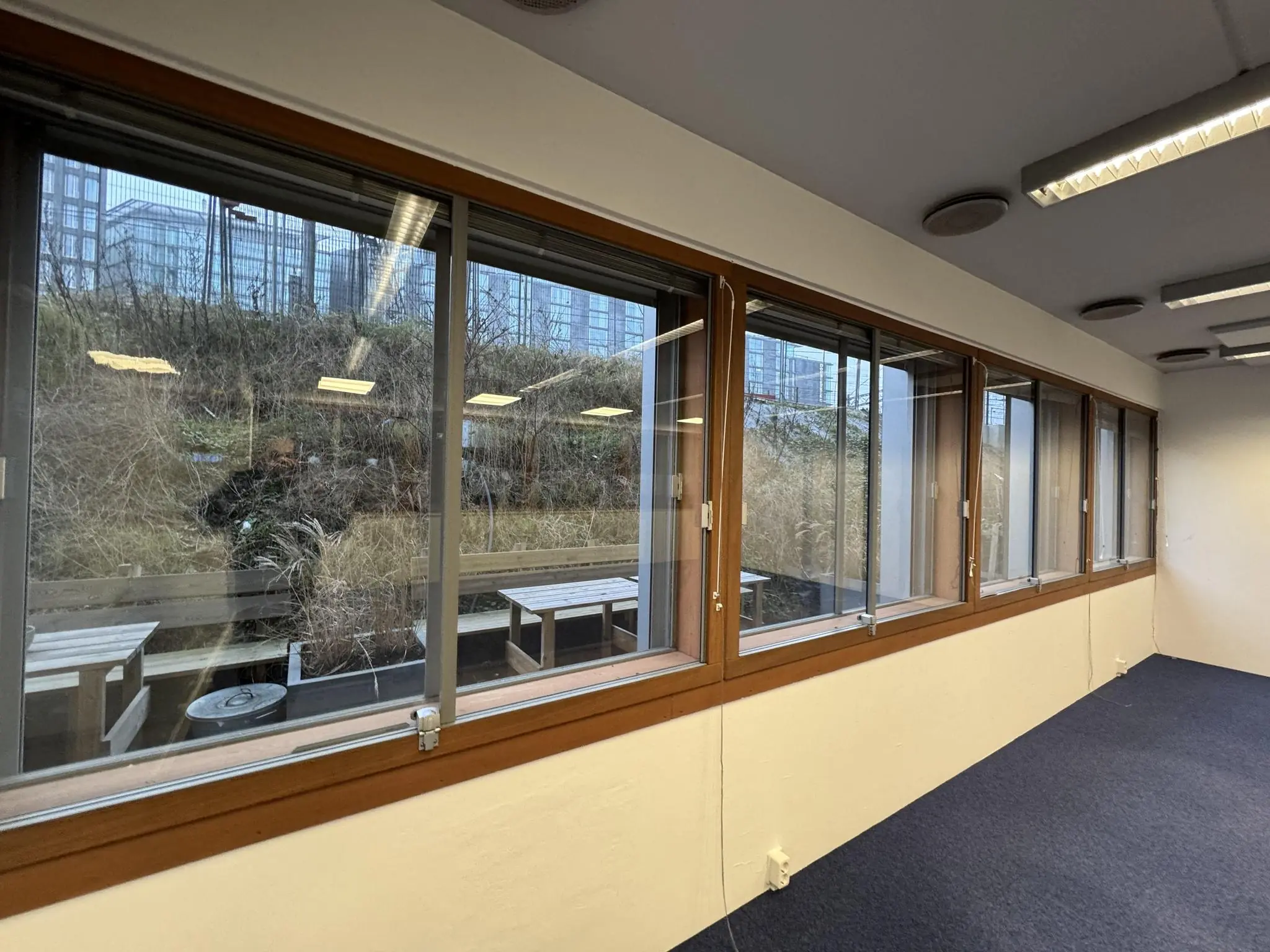 Kantoorruimte met grote ramen aan de De Ruijterkade, met uitzicht op een buitenterras en hoge gebouwen op de achtergrond.