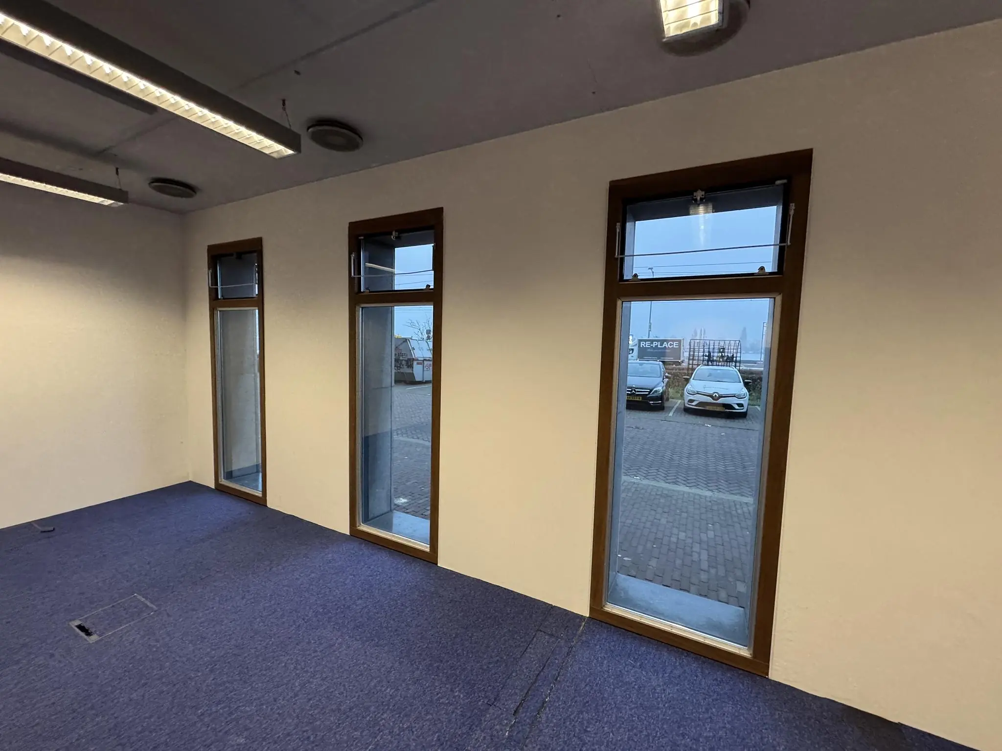 Leeg kantoor aan de De Ruijterkade met drie smalle ramen en zicht op geparkeerde auto's buiten.