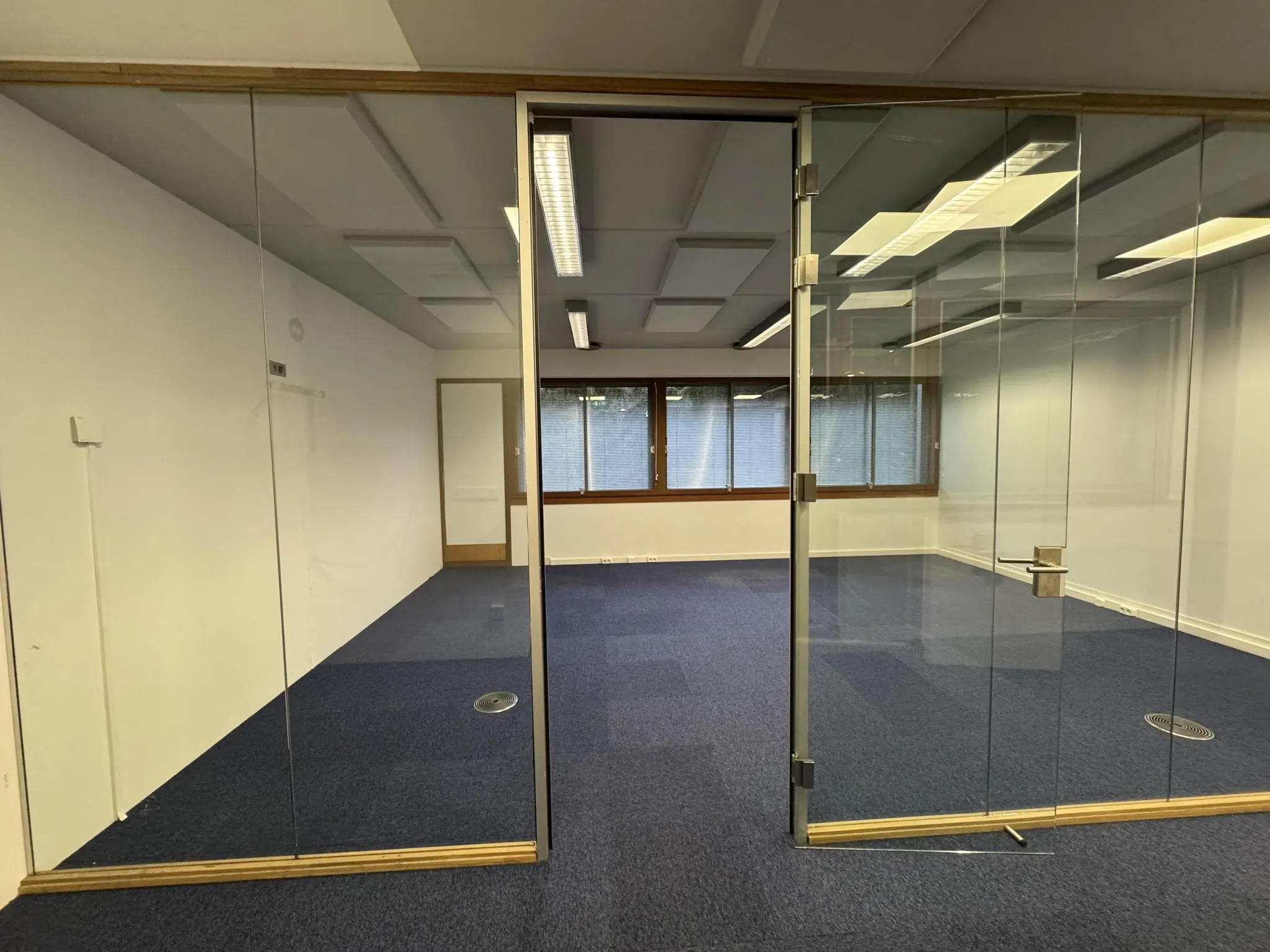 Leeg kantoorpand aan de De Ruijterkade met glazen wanden, blauwe vloerbedekking en grote ramen.