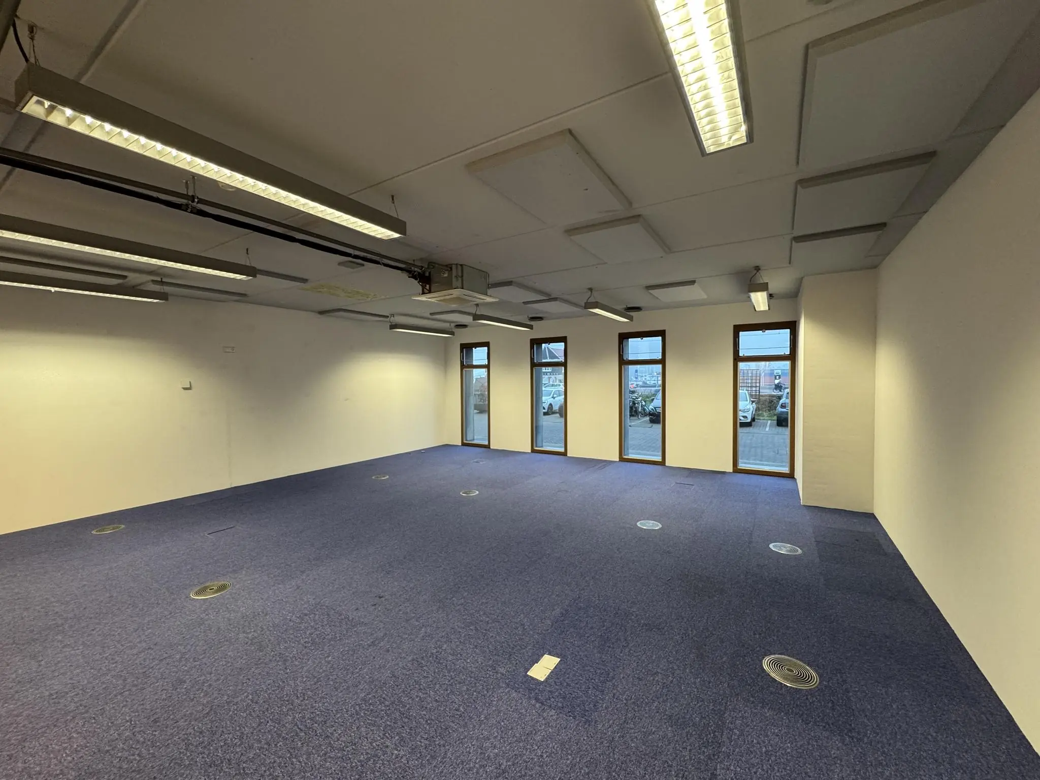 Leeg kantoorruimte aan de De Ruijterkade met blauwe vloerbedekking, witte muren en grote ramen aan de straatzijde.