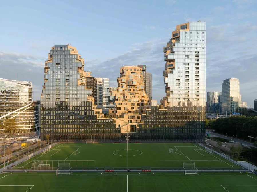 Zicht op het moderne gebouw Valley aan de Beethovenstraat in Amsterdam met een voetbalveld op de voorgrond.