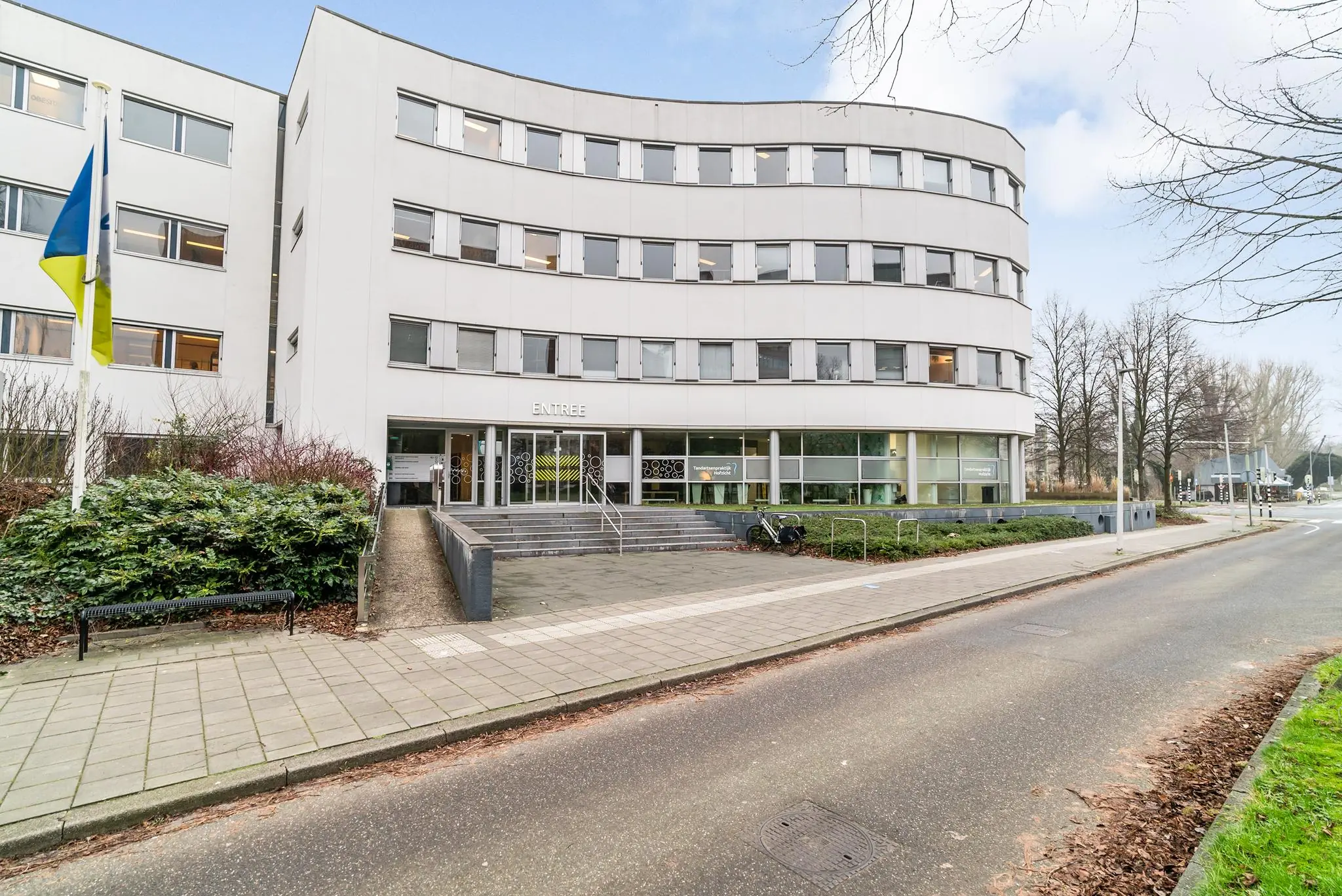 Vooraanzicht van een modern kantoorgebouw aan de Bordewijklaan met de ingang en vlag op de voorgrond.