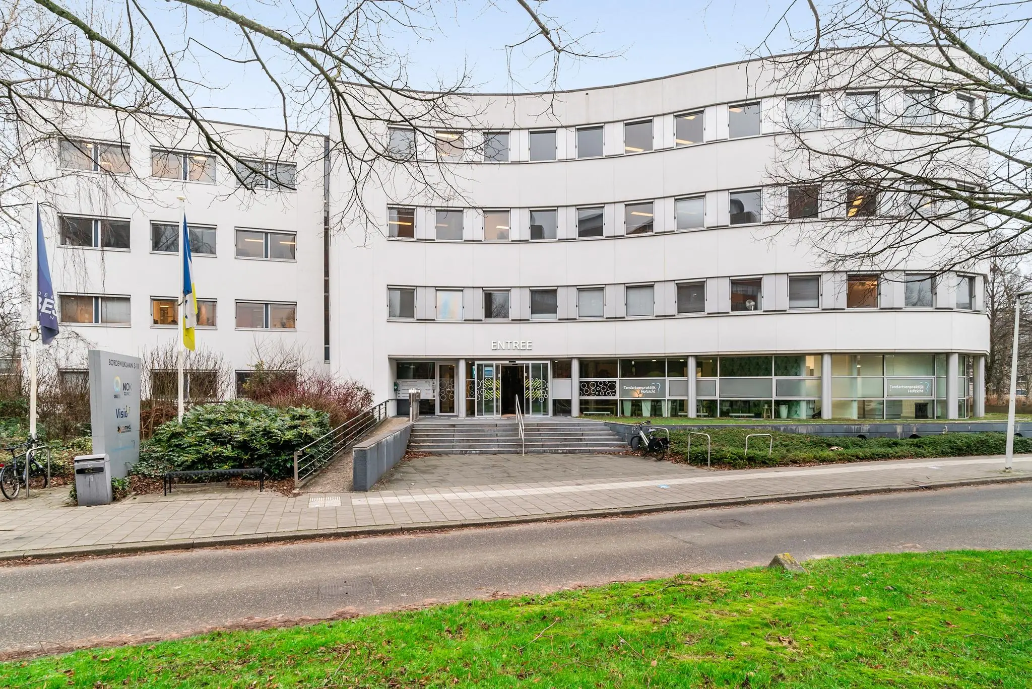 Wit kantoorgebouw aan de Bordewijklaan met de hoofdingang en meerdere vlaggen en bedrijfsnaamborden zichtbaar.