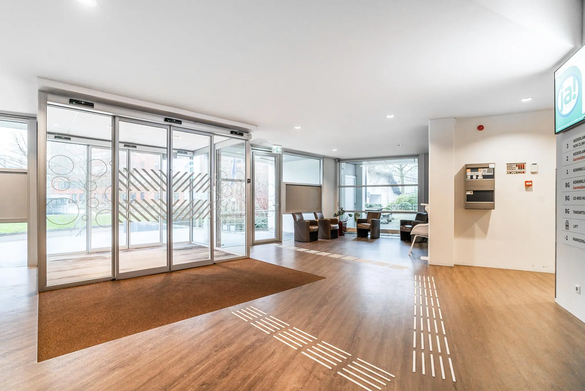Moderne entreehal van een gebouw aan de Bordewijklaan met automatische schuifdeuren, wachtruimte en geleidelijnen op de vloer.